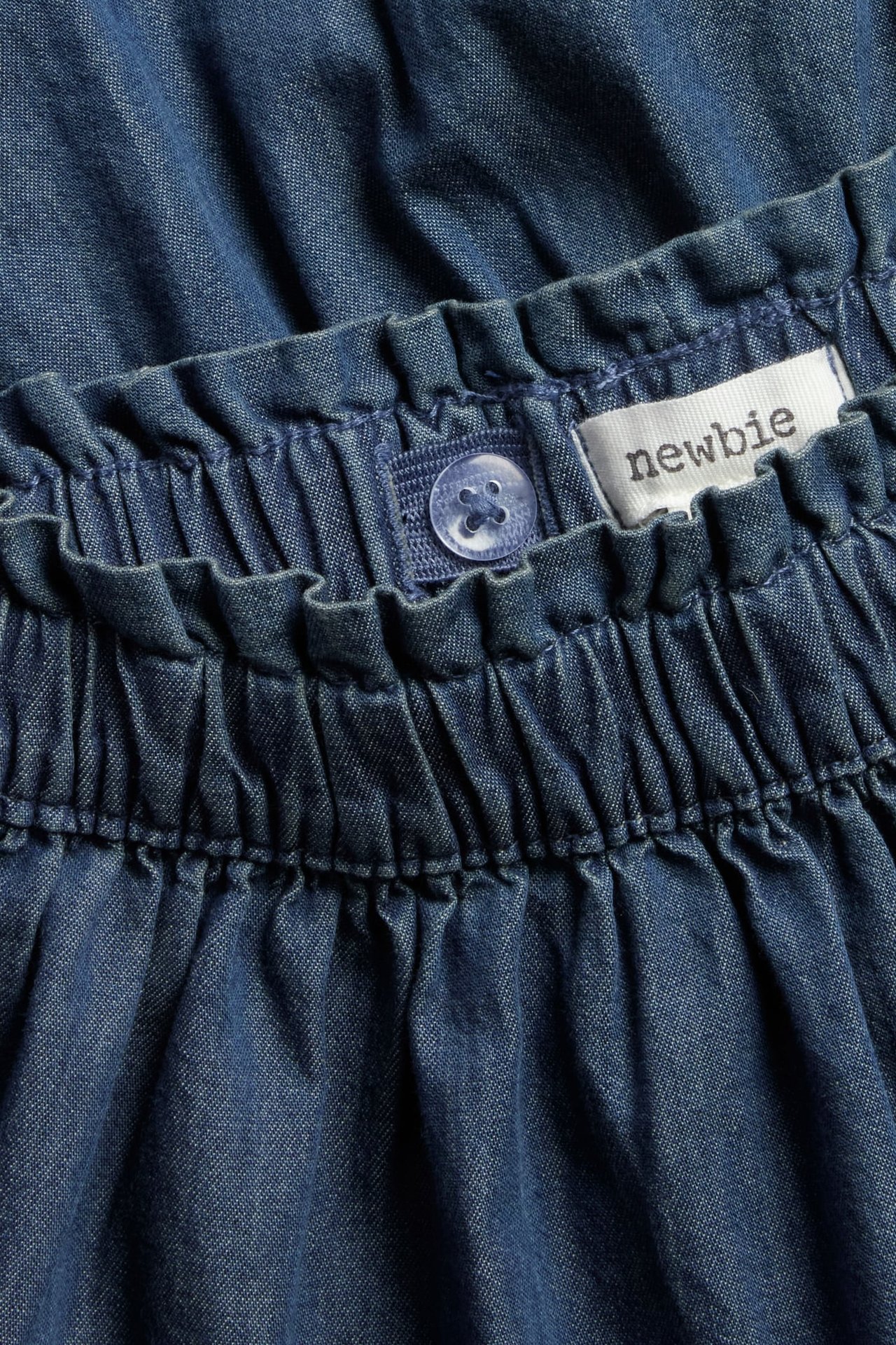 Nahaufnahme eines blauen Jeansrocks für Kinder mit elastischem Bund, verstellbarem Knopf und Newbie-Etikett.