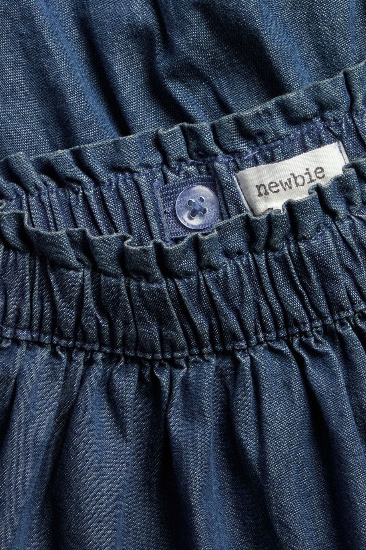 Nahaufnahme eines blauen Jeansrocks für Kinder mit elastischem Bund, verstellbarem Knopf und Newbie-Etikett.