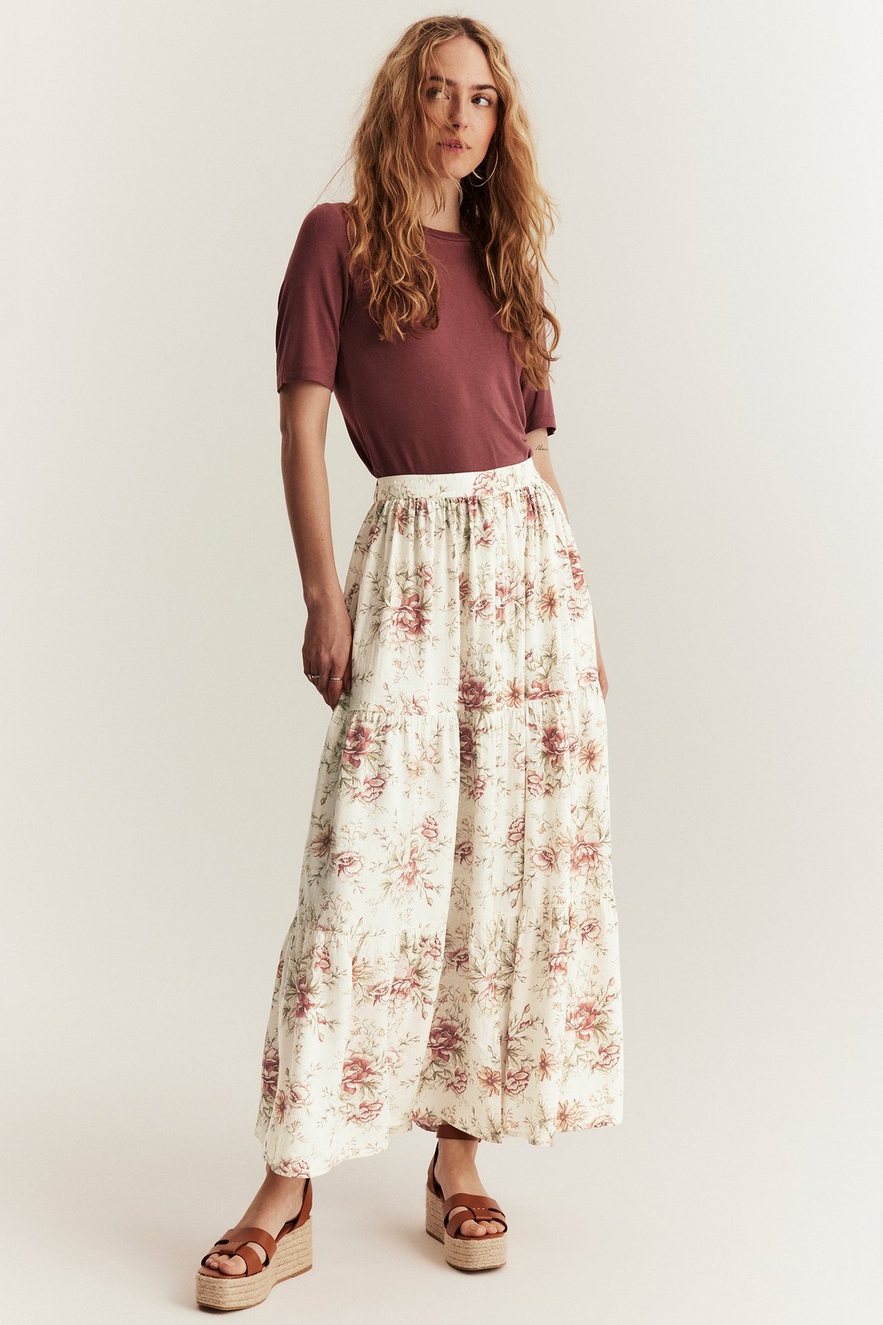Front view: Woman in off-white floral viscose long skirt, dark red t-shirt, and brown wedge sandals.