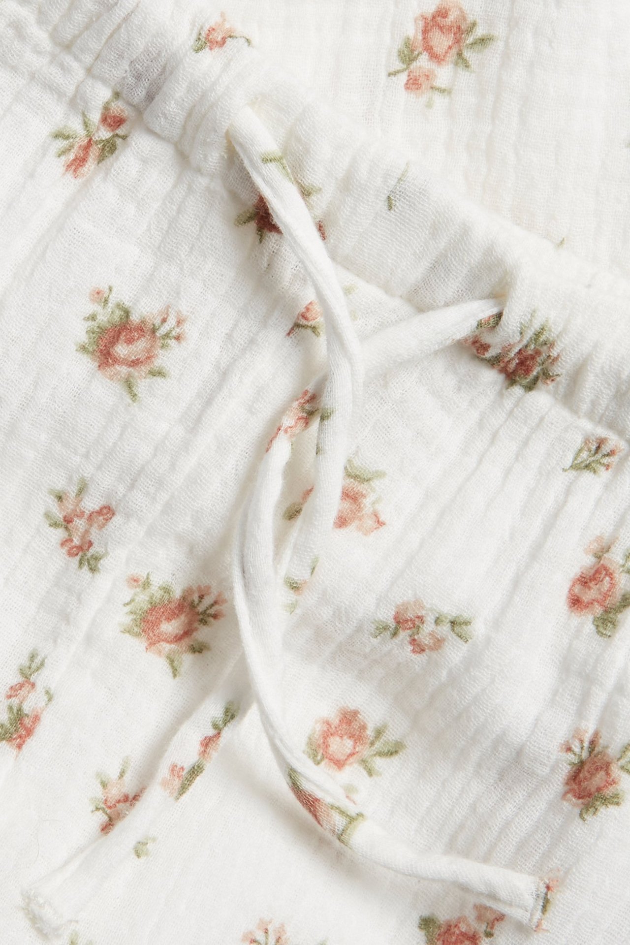 Nahaufnahme von cremeweißen gewebten Baumwoll-Puffhosen mit rosa Blumenmuster und Kordelzug.
