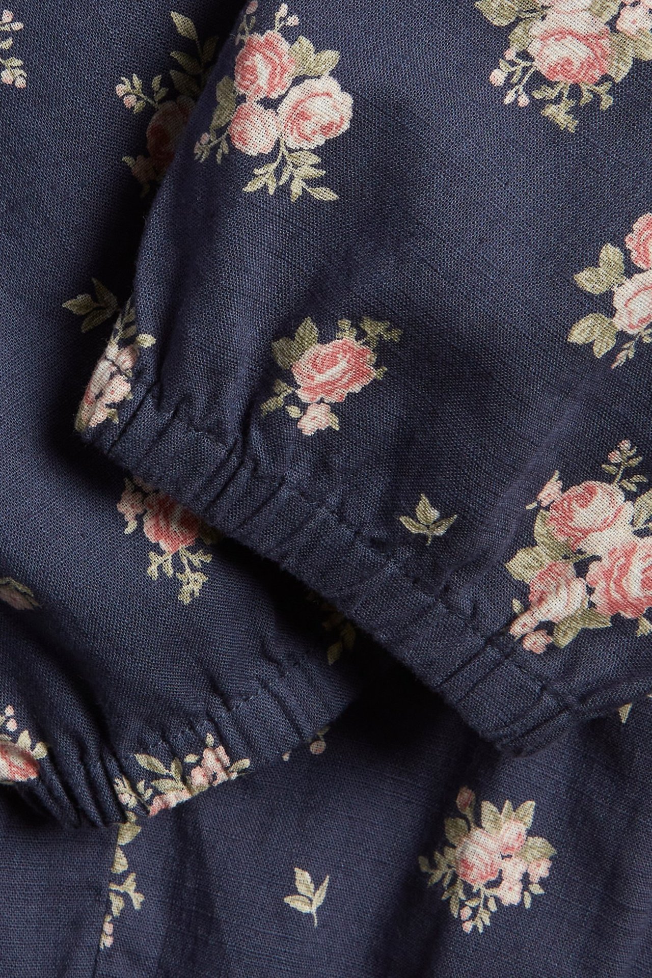 Close-up of dark blue cotton woven trousers with a pink floral pattern and elasticated leg opening.