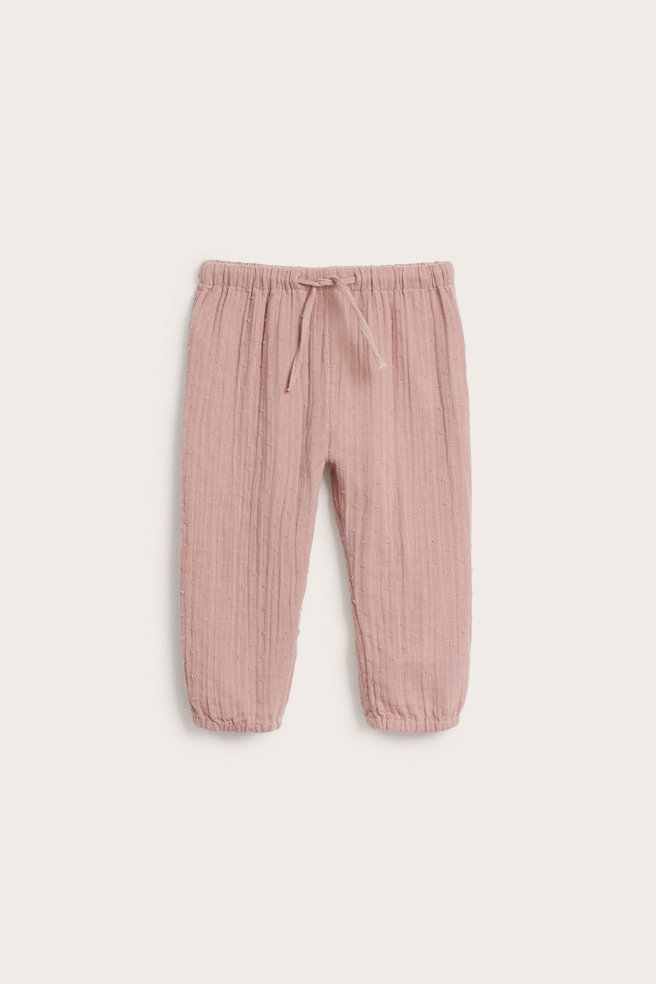 Front view of pink woven baby pants with a textured surface, elastic waist, and drawstring.