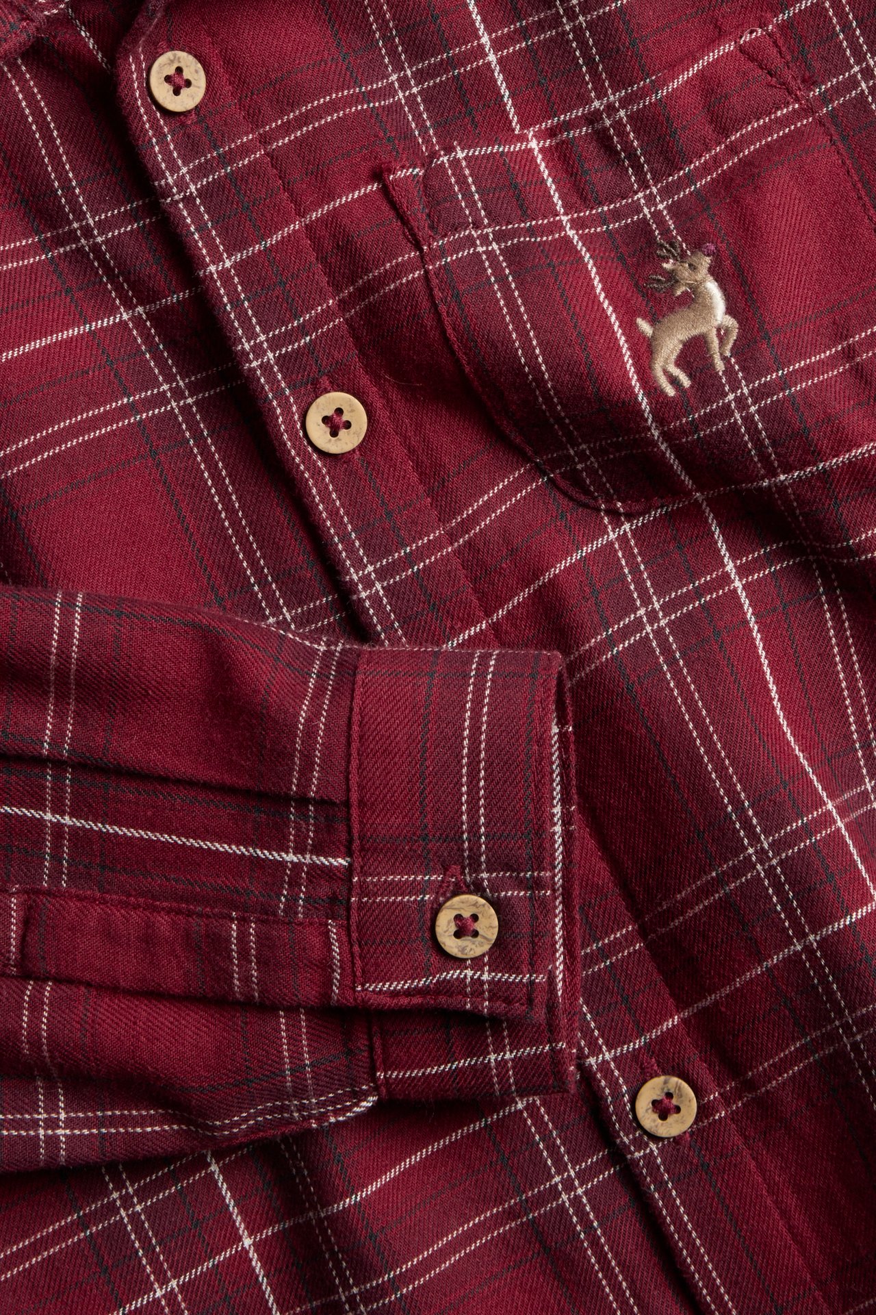 Close-up of a red plaid cotton shirt with front buttons, a chest pocket, and deer embroidery.