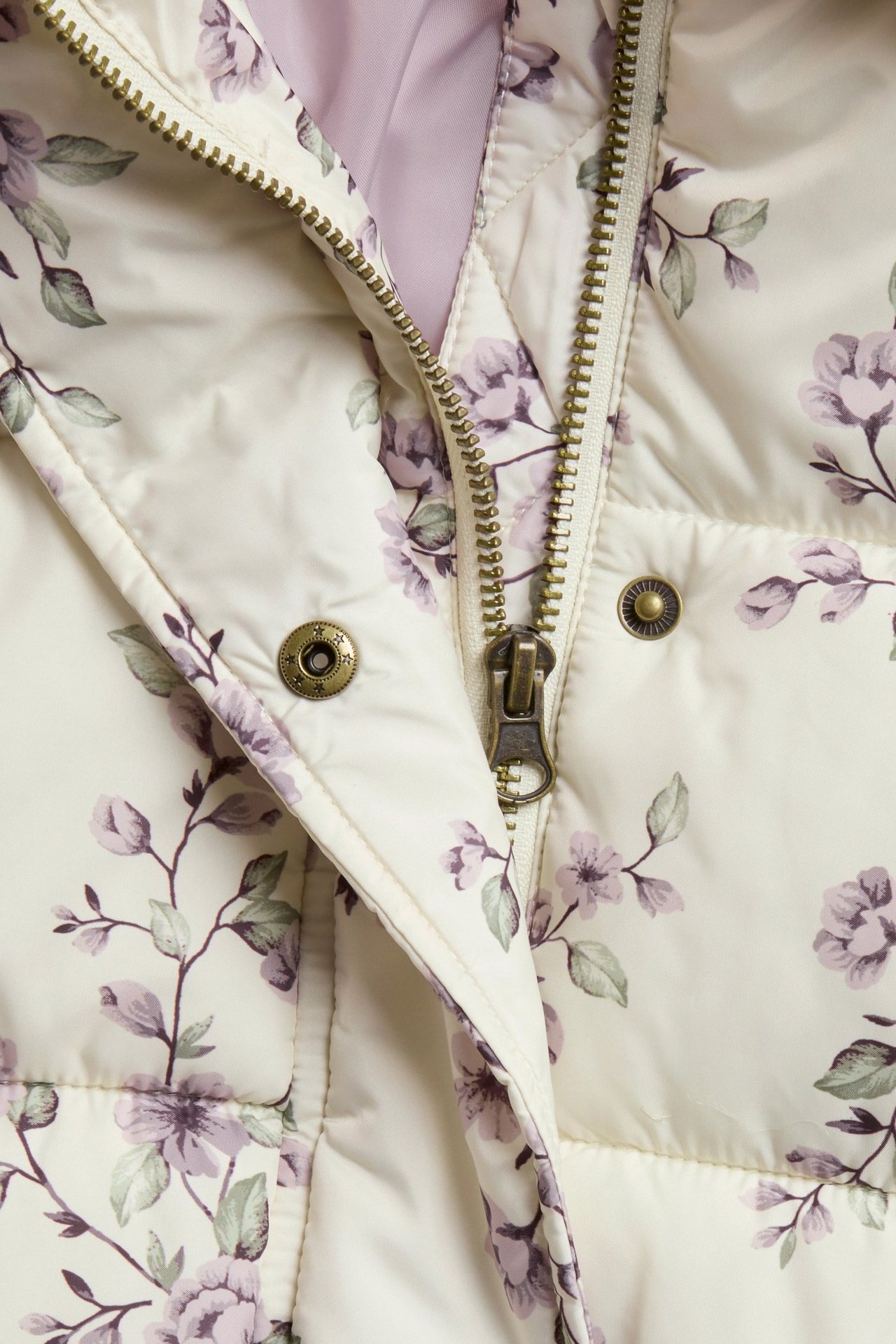 Close-up front view: light beige padded jacket with purple floral pattern, zipper and snap buttons.