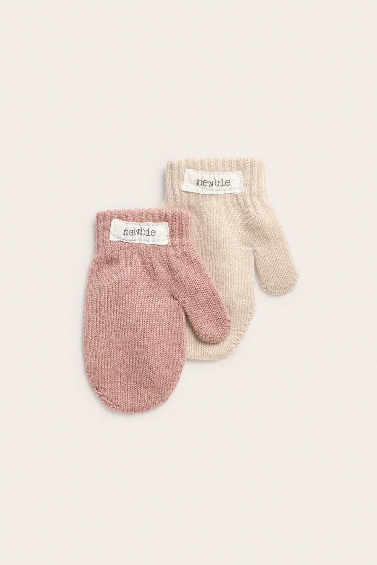 Nahaufnahme von rosa und hellbeigen gestrickten Babyhandschuhen, beide mit 'newbie'-Etiketten.