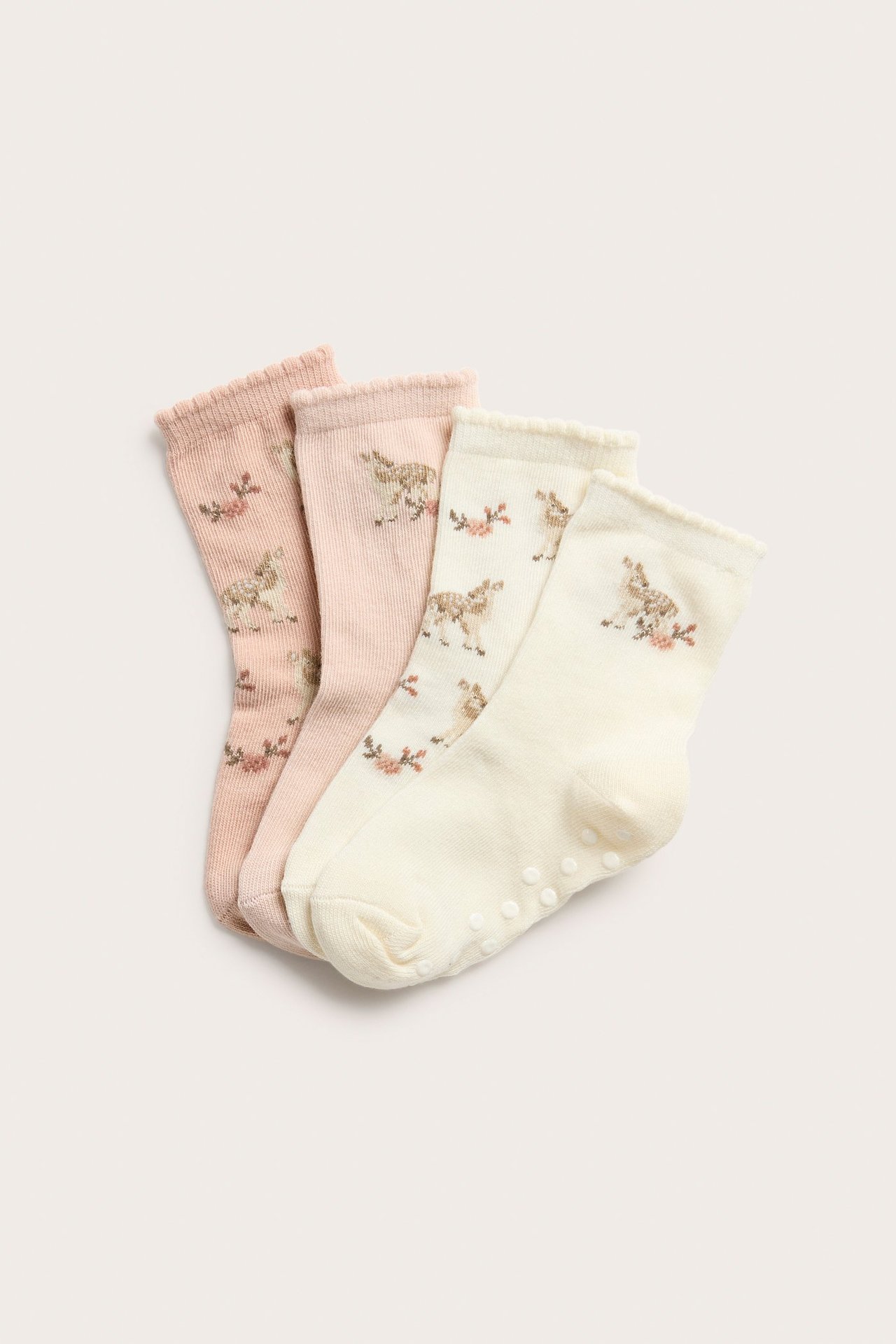 Vier gemusterte Socken: zwei hellrosa, zwei cremefarbene, mit Hirsch- und Blumendruck. Eine hat Antirutsch-Noppen.