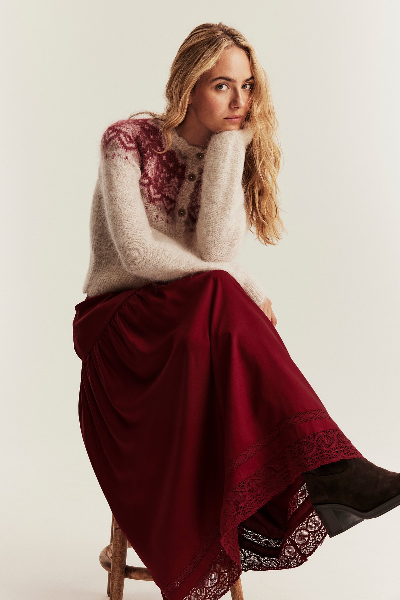 Vorderansicht einer sitzenden Frau mit rotem Viskose-Midirock mit Spitze und beiger gemusterter Strickjacke.