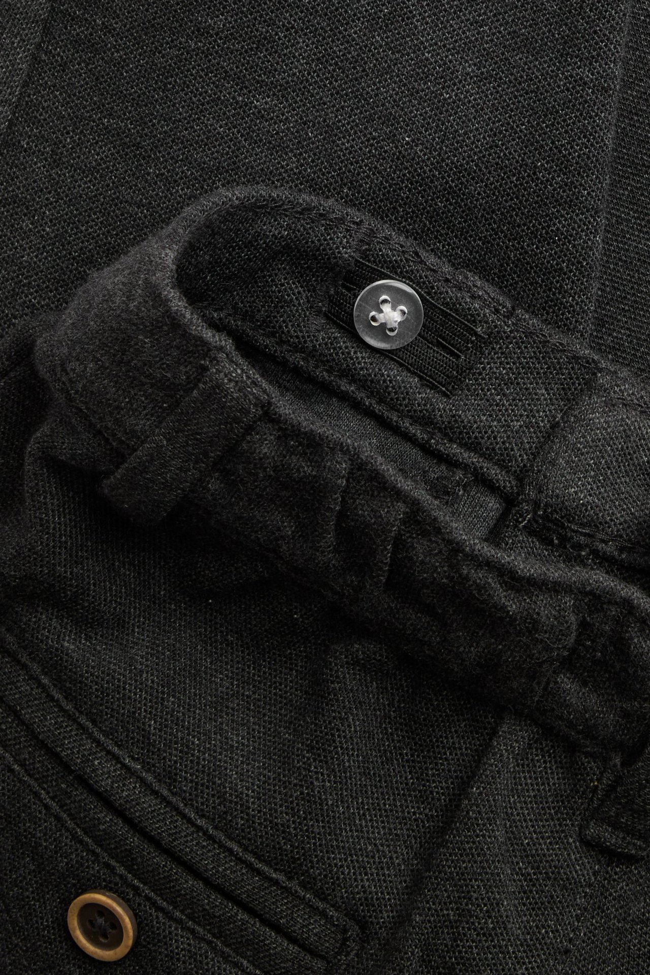 Nahaufnahme von dunkelgrauen Melange-Kinderhosen mit Knopf vorne, verstellbarem Gummiband und Tasche.