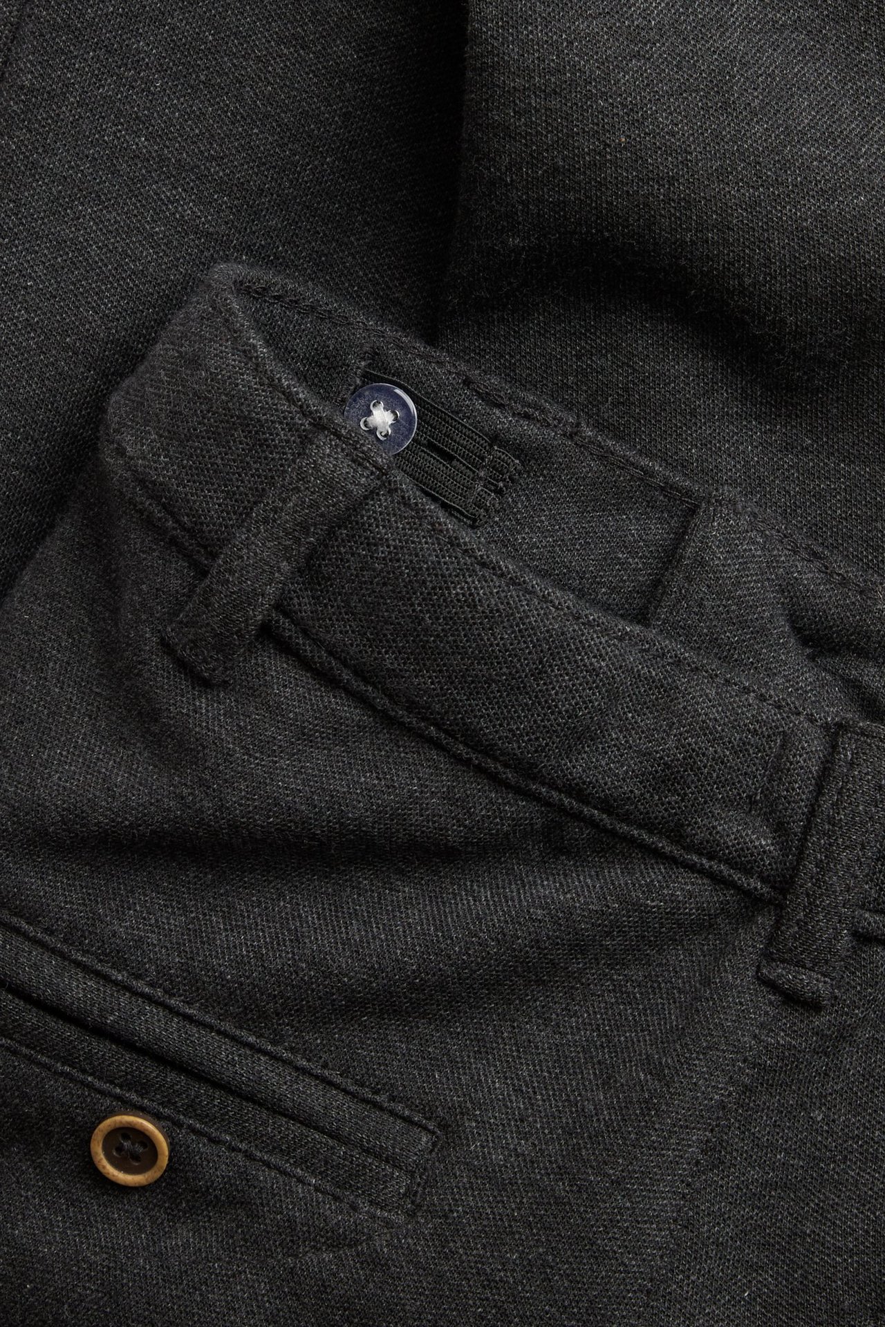 Nahaufnahme einer dunkelgrau melierten Kinderhose mit blauem Bundknopf und dekorativem Taschenknopf.