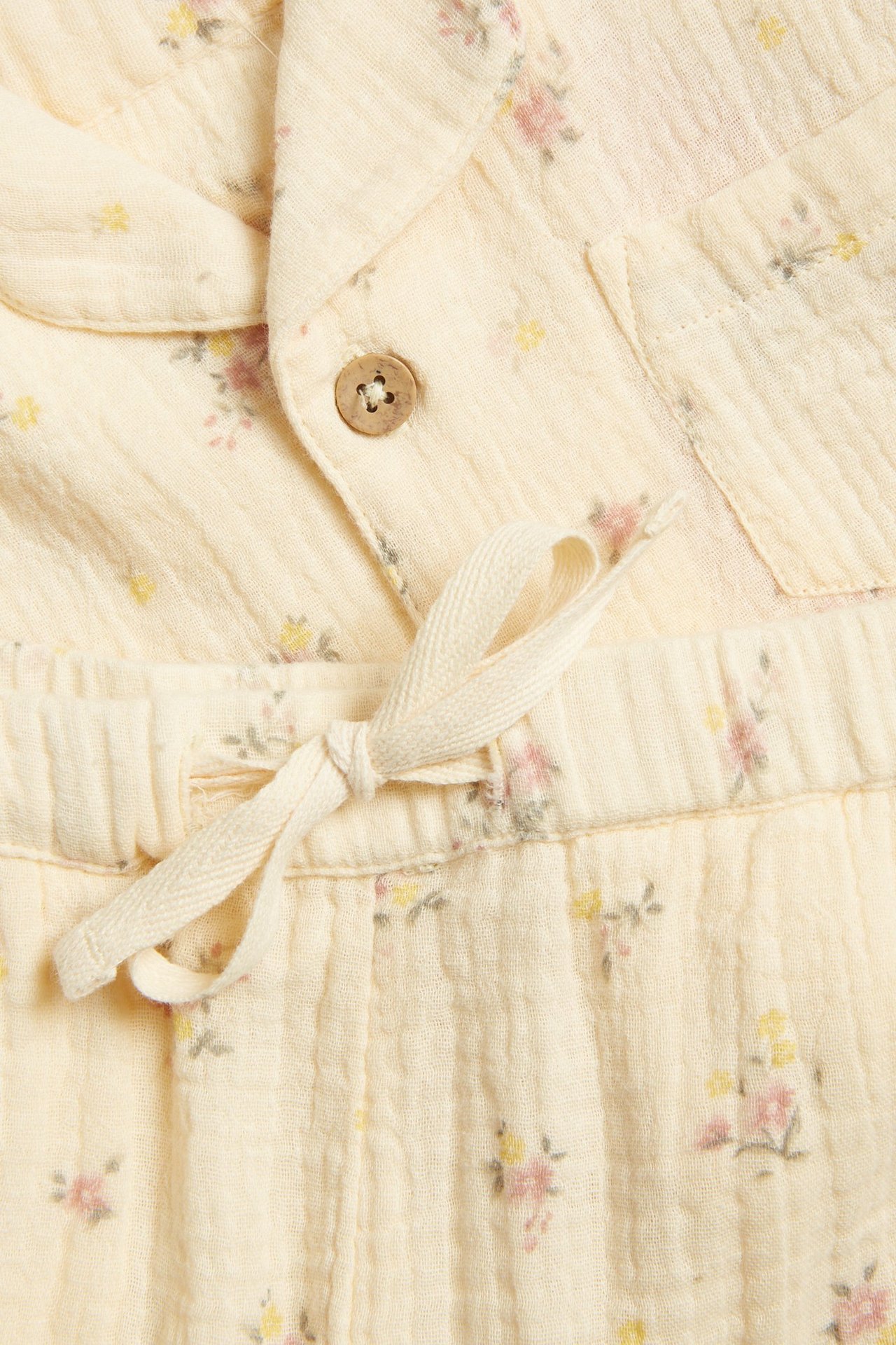 Nahaufnahme eines hellgelben geblümten Baumwoll-Pyjamas mit geknöpftem Hemd und Kordelzug-Hose.