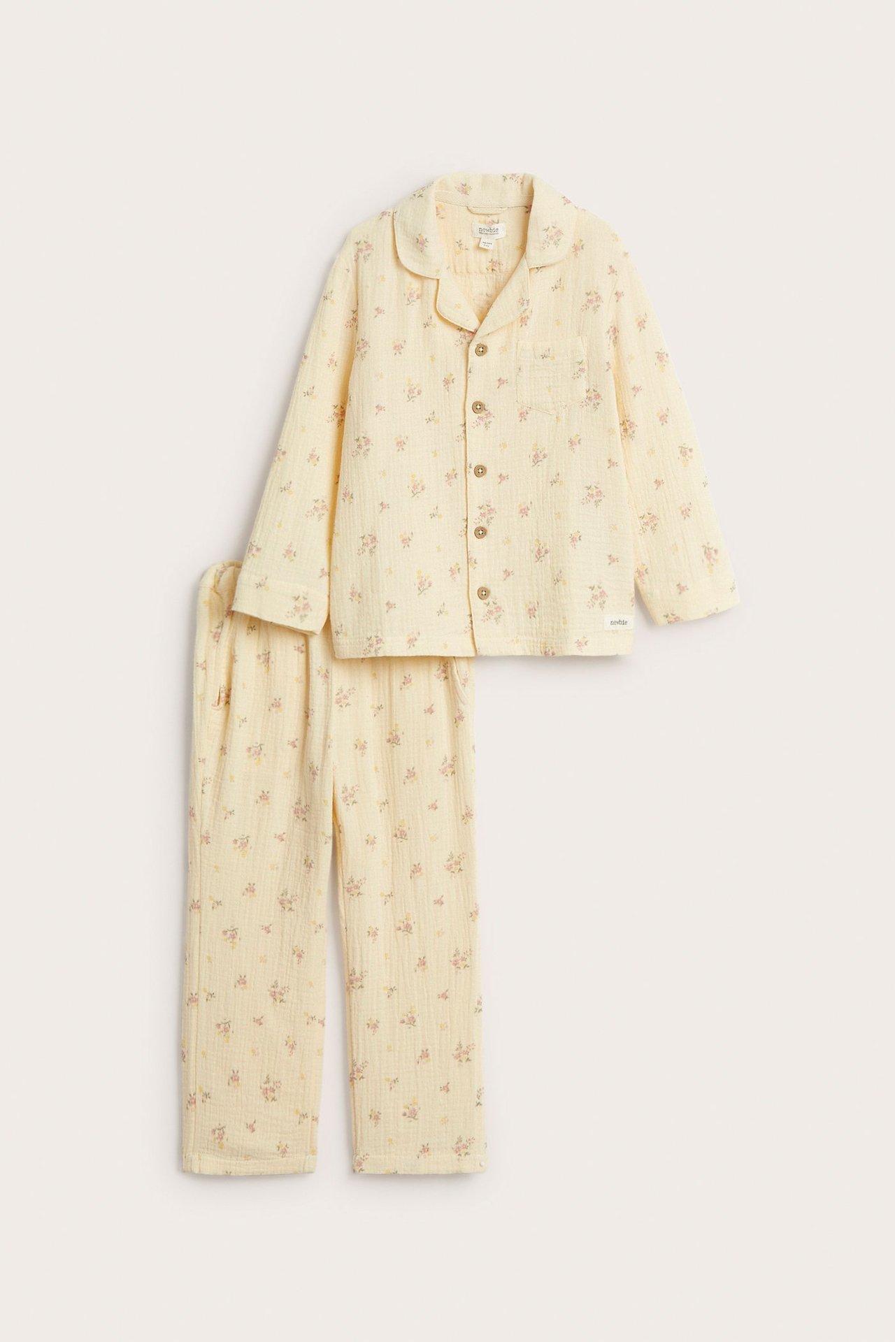 Vorderansicht: Hellgelber zweiteiliger Baumwollpyjama mit Blumenmuster. Oberteil mit Kragen, Knöpfen; Hose mit Kordelzug.