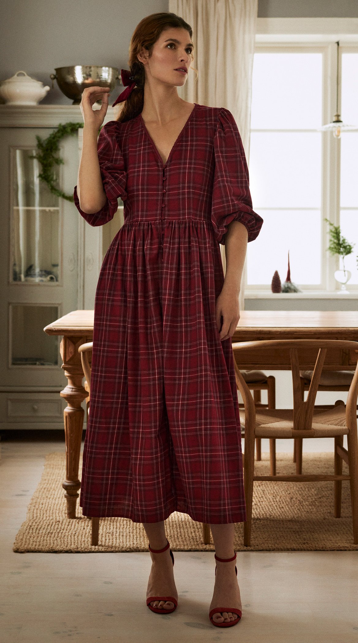 Front view of woman in red plaid midi dress with puff sleeves, front buttons, and red sandals.