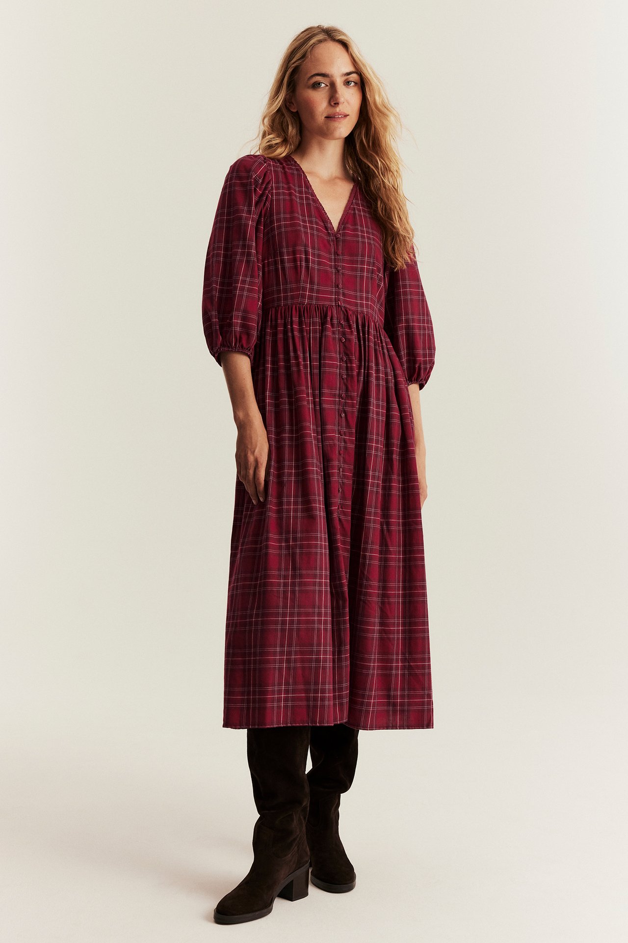 Vorderansicht einer Frau in einem roten karierten Baumwoll-Midikleid mit Puffärmeln und dunkelbraunen Stiefeln.