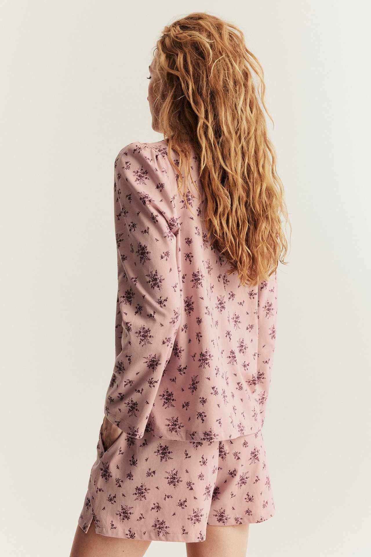 Rückenansicht einer Frau in einem rosa geblümten Baumwoll-Pyjama-Set mit Langarm-Oberteil und Shorts.