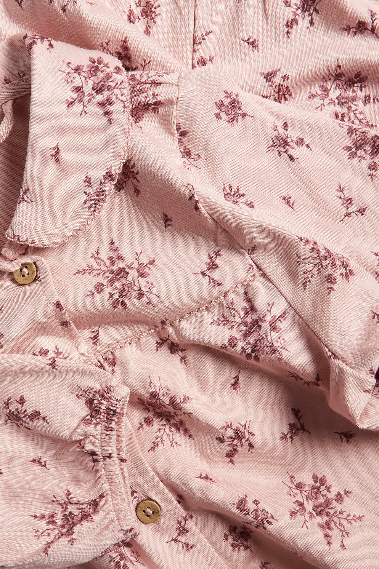 Nahaufnahme eines rosa geblümten Baumwolljersey-Pyjamas mit Kragen, Knöpfen und elastischen Ärmelbündchen.