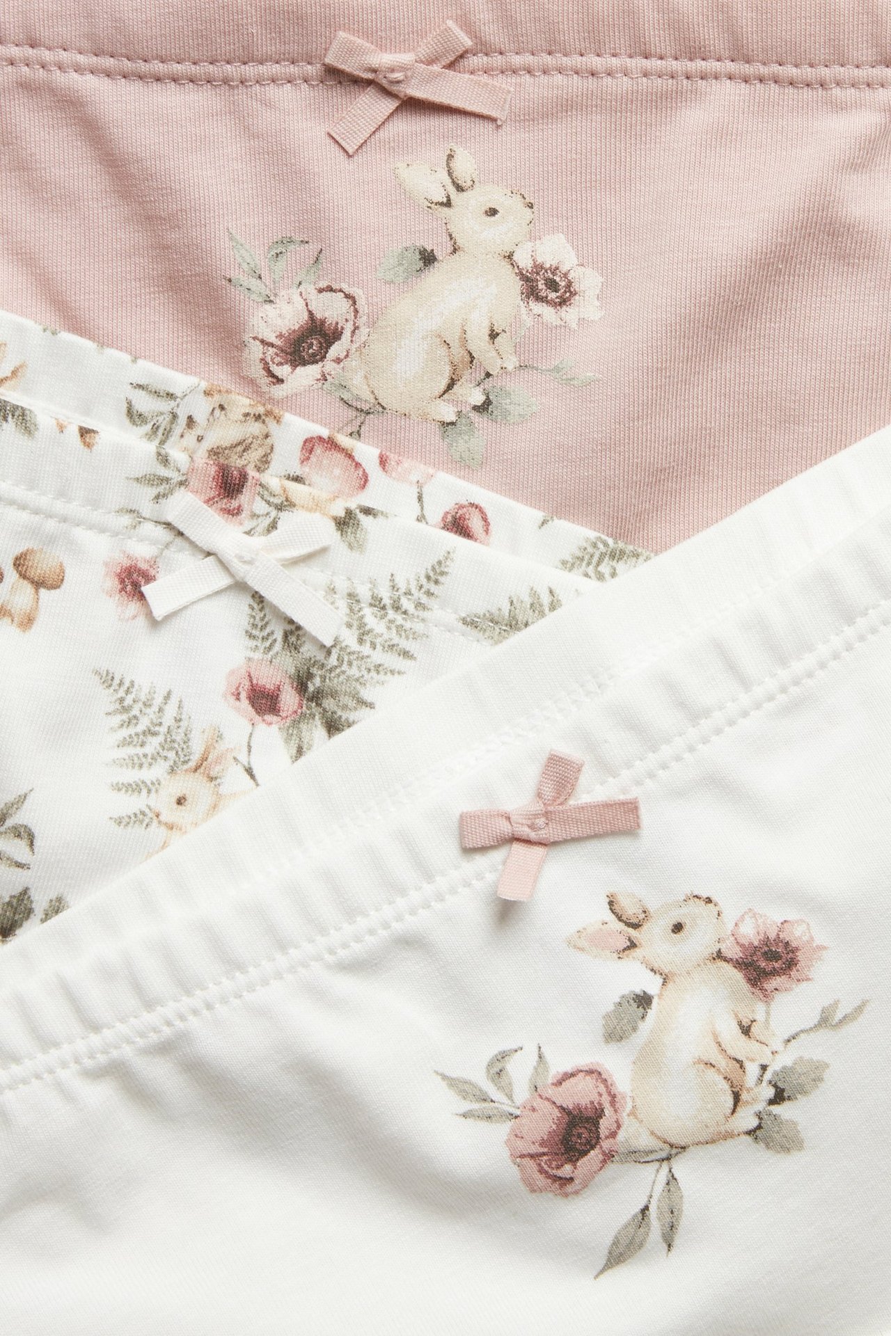 Nahaufnahme von drei Kinder-Boxershorts: eine rosa, zwei cremefarbene, alle mit Blumen-Hasen-Prints und Schleifen.