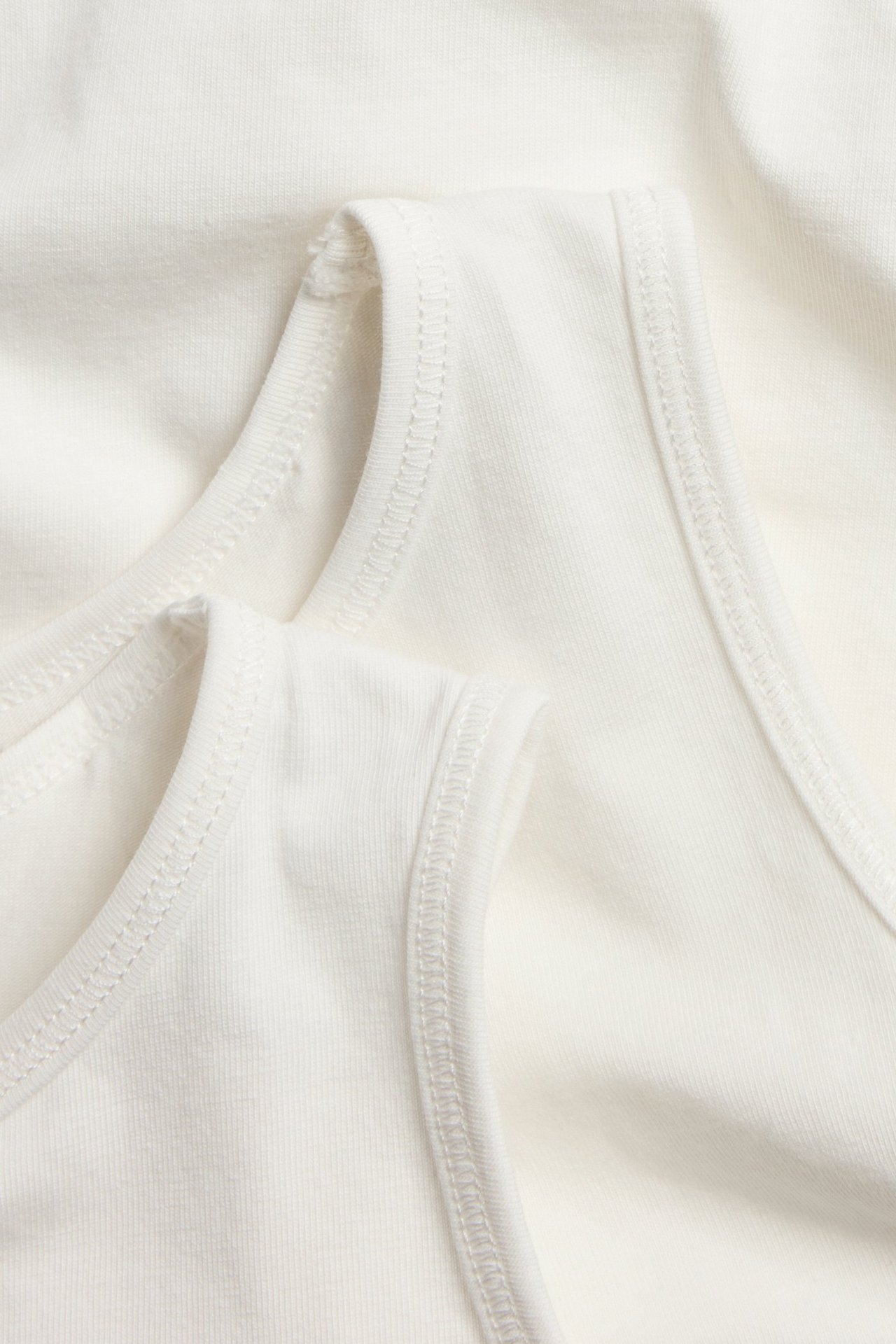 Nahaufnahme von zwei einfarbigen cremeweißen Baumwoll-Tanktops mit sichtbaren Nähten.