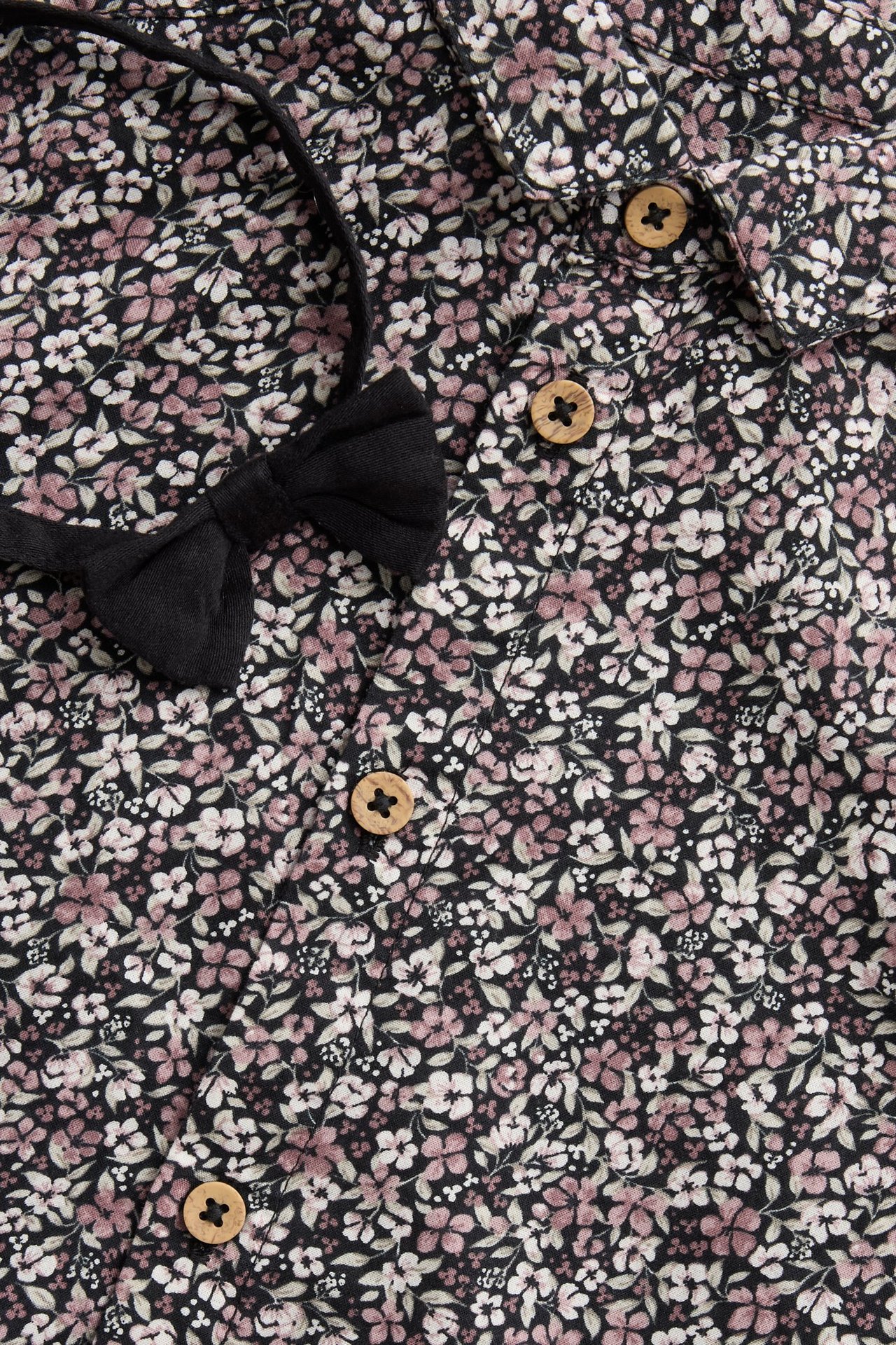 Close-up of a black floral cotton shirt with wooden buttons and a black bow tie.