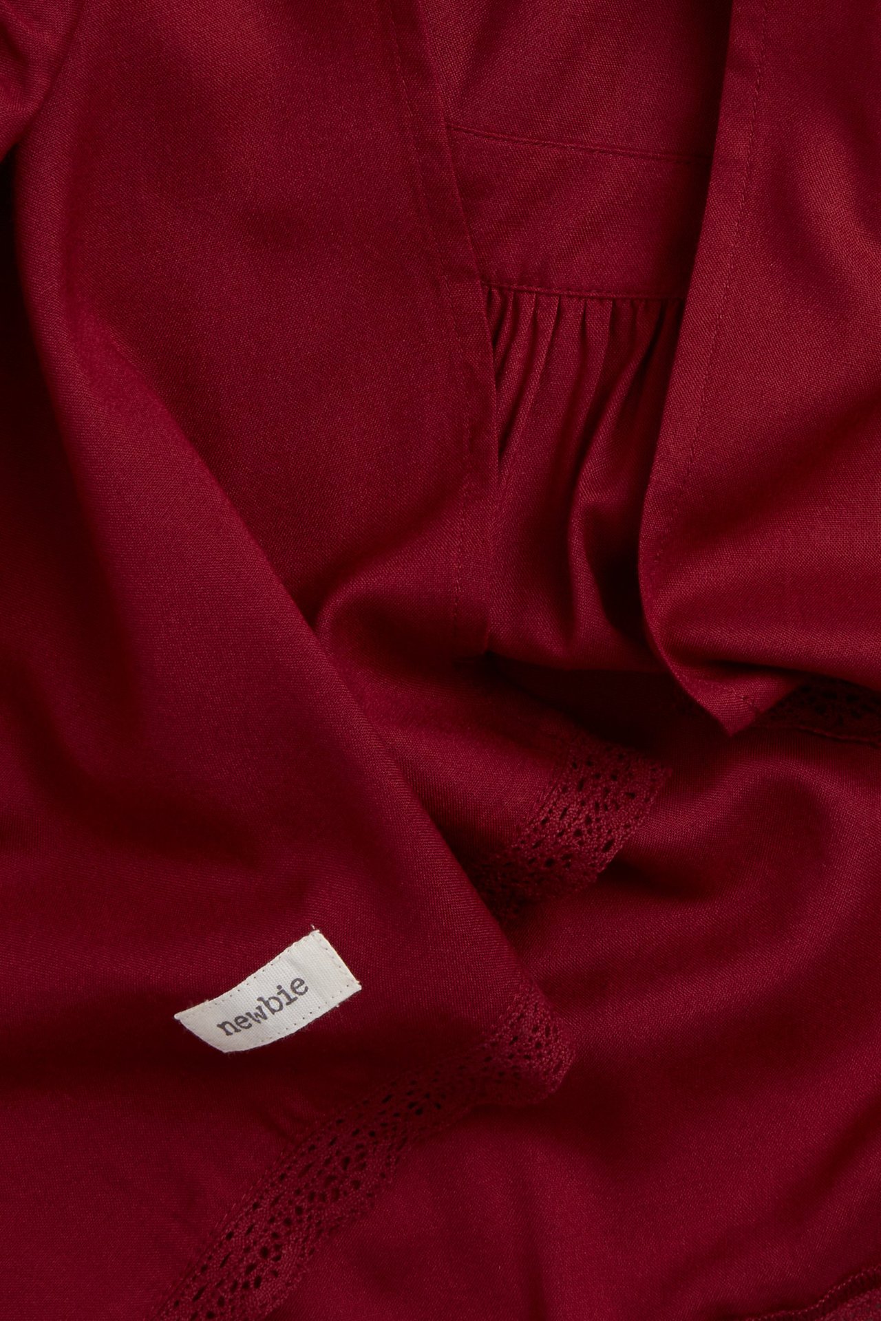 Close-up of a deep red solid viscose apron with gathers and delicate lace trim.