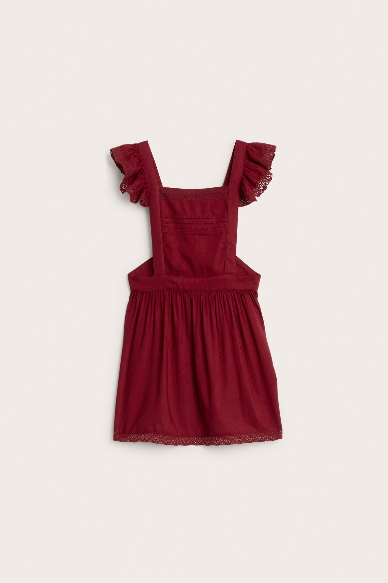 Front view of a red kid's viscose apron dress with ruffled lace shoulder straps and lace trim.
