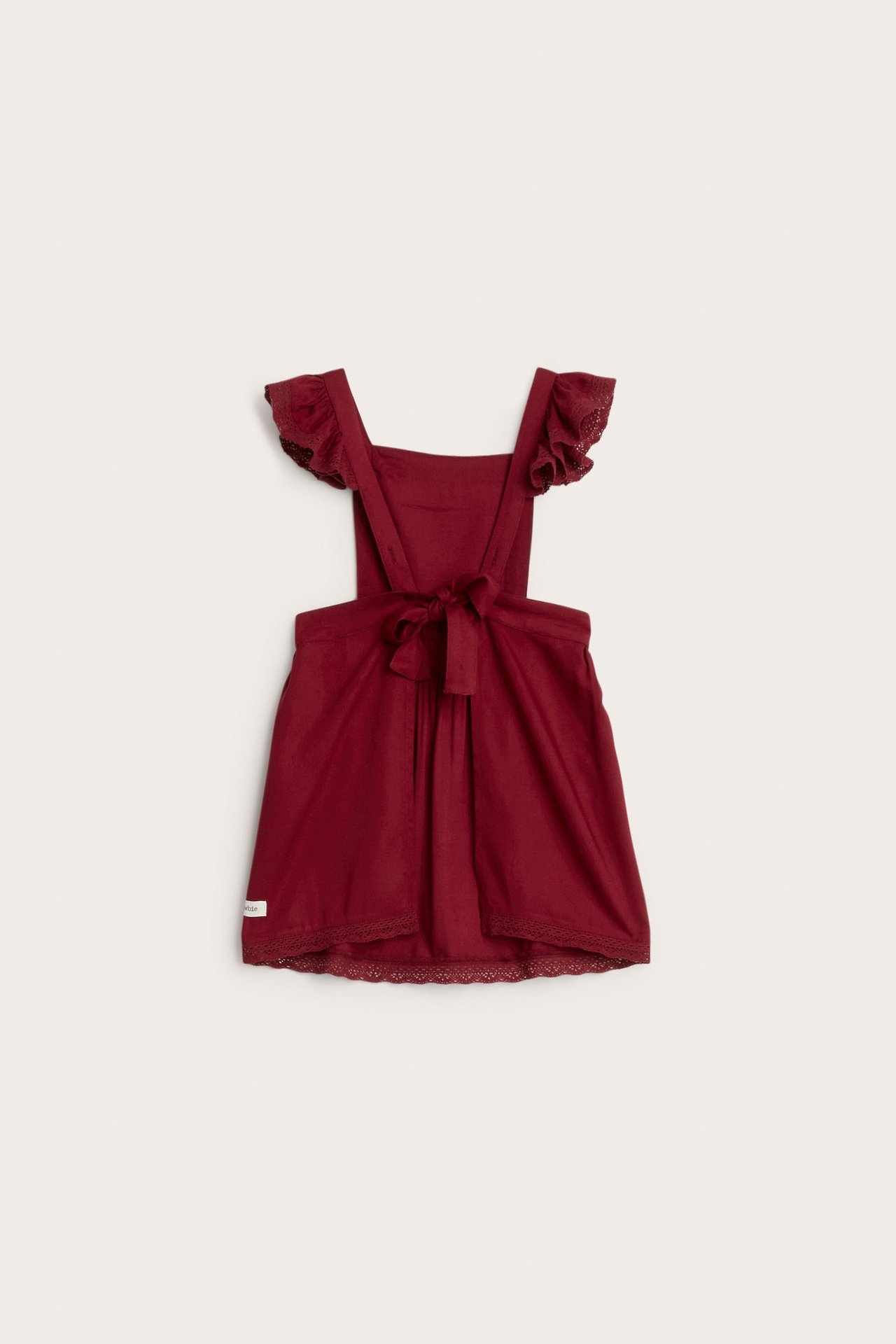 Front view of a kid's solid red viscose apron dress with ruffled shoulder straps and a tied back.