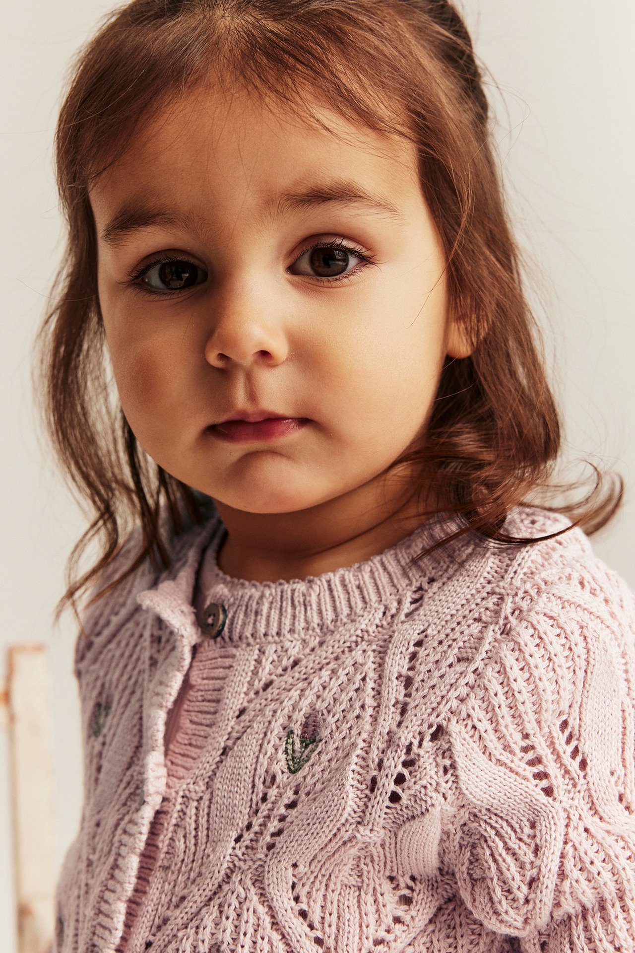 Nahaufnahme von vorne eines Kindes in einer hellrosa Baumwollstrickjacke mit gestickten Blumen.