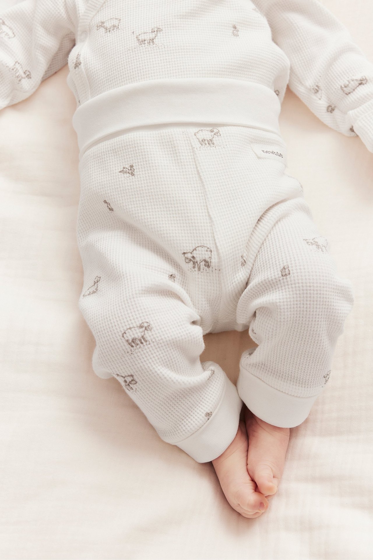 Nahaufnahme eines Babys in cremeweißen Waffelstrick-Leggings mit Lamm-Muster und breiten Bündchen.