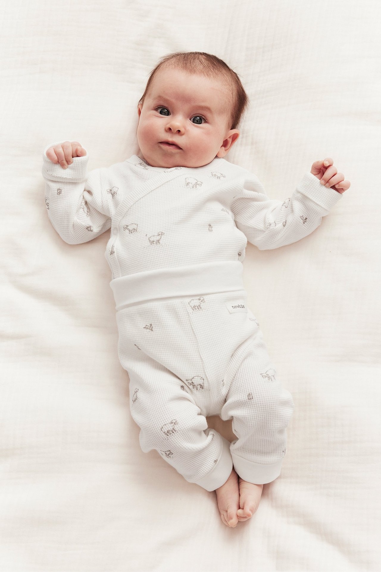 Draufsicht auf ein Baby in cremeweißen Waffel-Leggings und passendem Wickeloberteil mit Lamm-Muster.