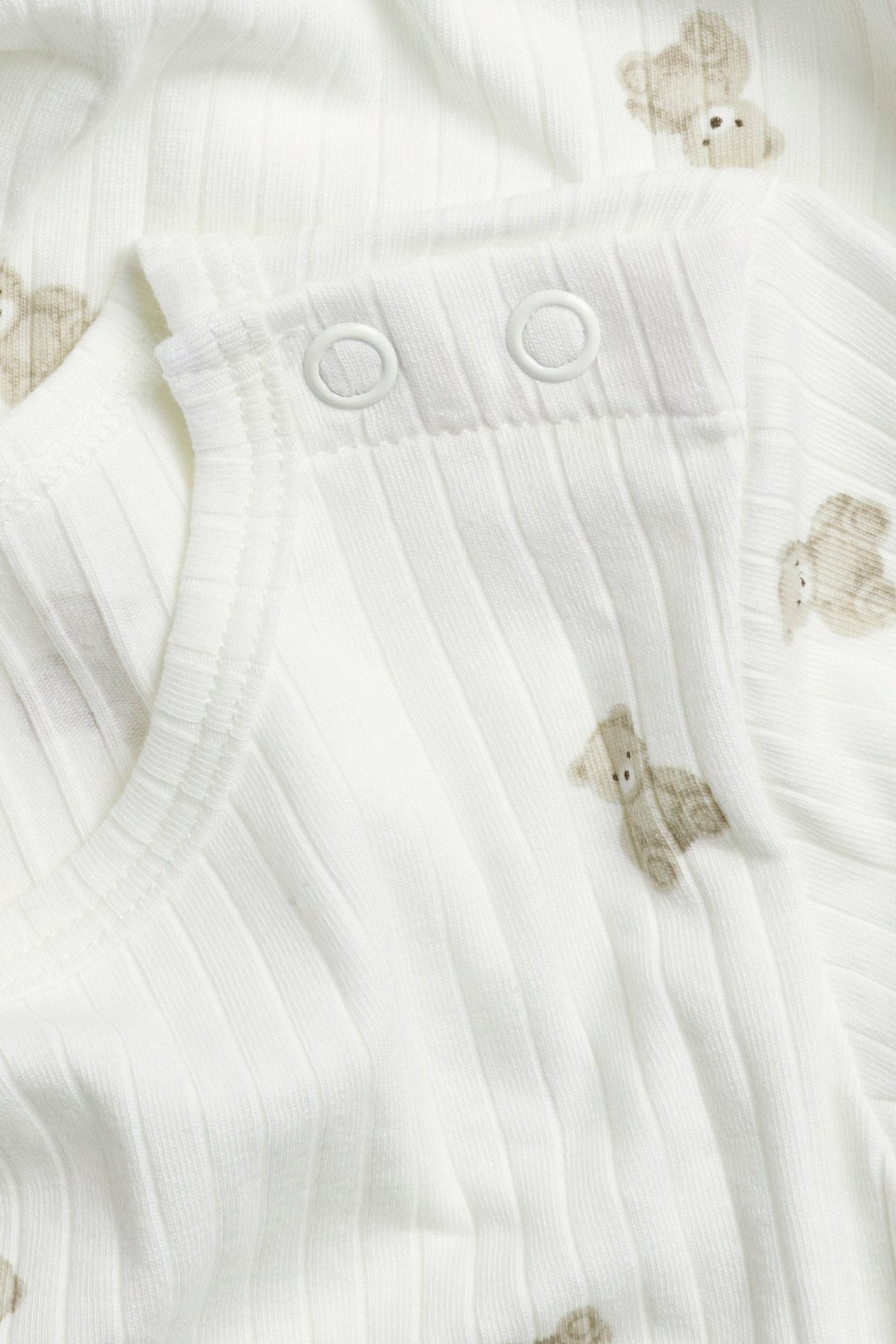 Nahaufnahme eines cremefarbenen gerippten Langarm-Babybodys mit Teddybärmuster und Schulter-Druckknöpfen.