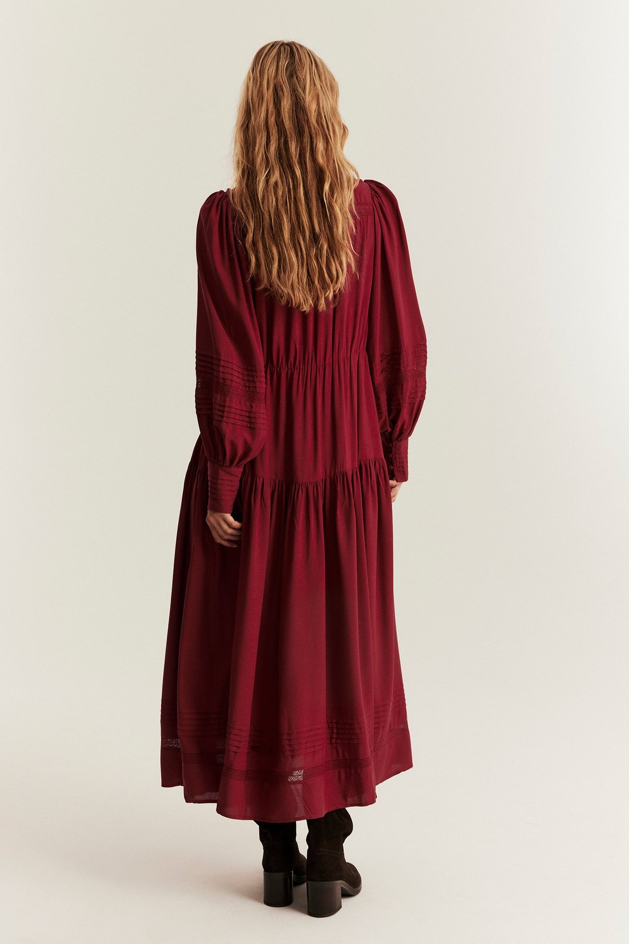 Rückenansicht einer Frau in langem rotem Viskosekleid mit Spitze und Biesen, dazu dunkelbraune Stiefeletten.