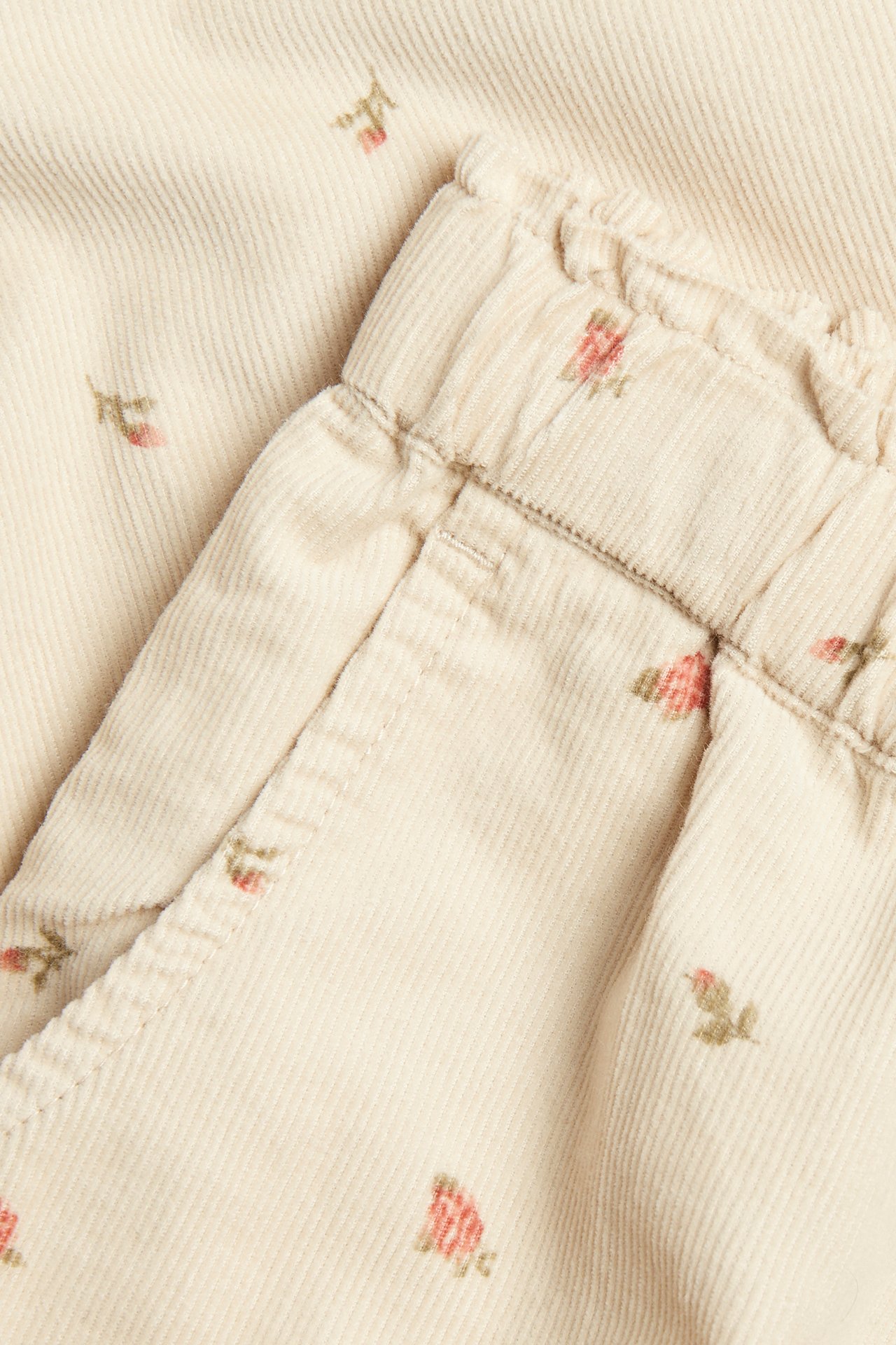 Close-up of beige corduroy trousers with small floral print and elasticated waist.