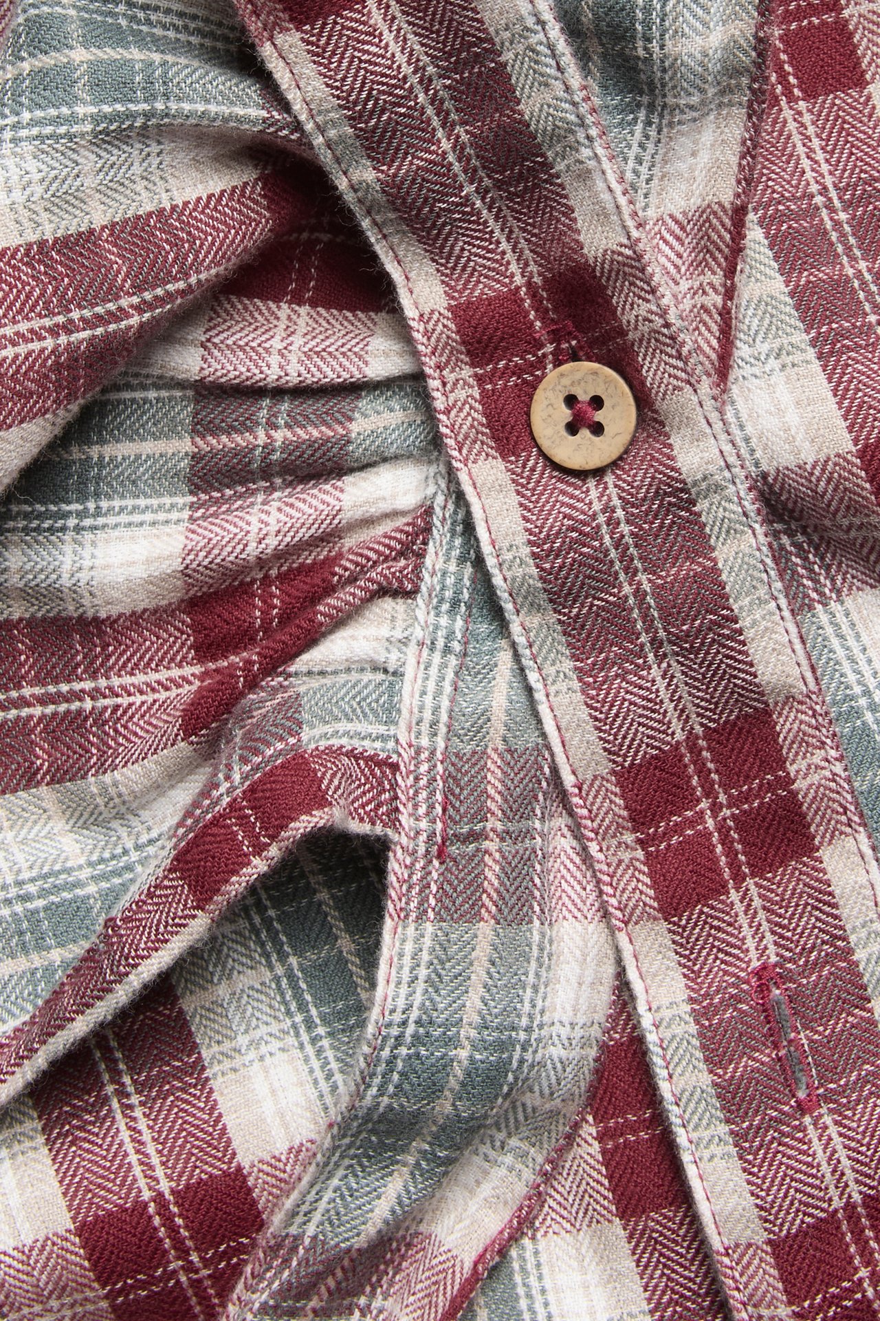 Nahaufnahme: Weinrote, beige und graue karierte Baumwollschürze, Rüschendetail, Holzknopf.