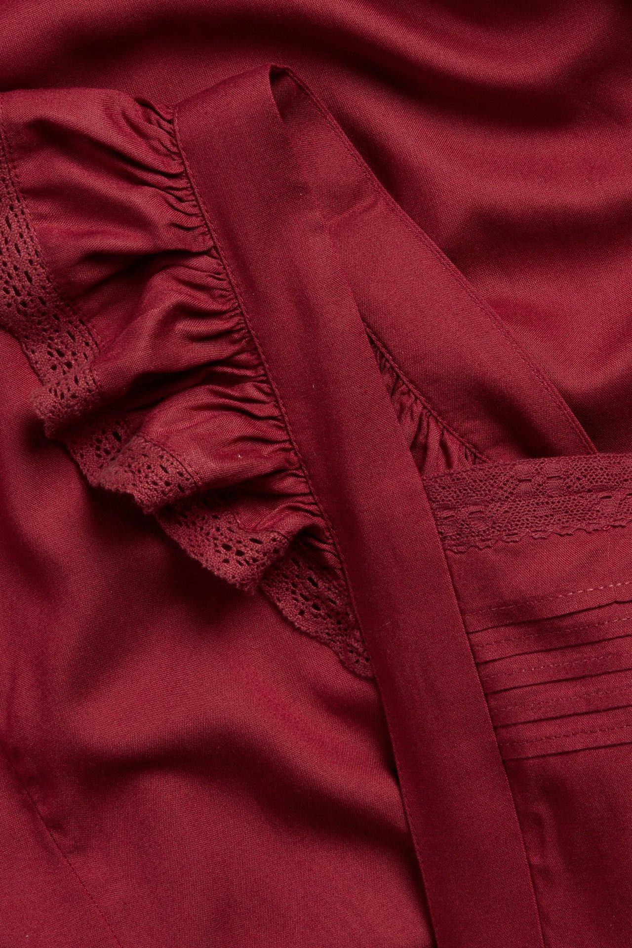 Close-up of a red viscose apron with ruffles on straps, decorative lace, and front pleat details.