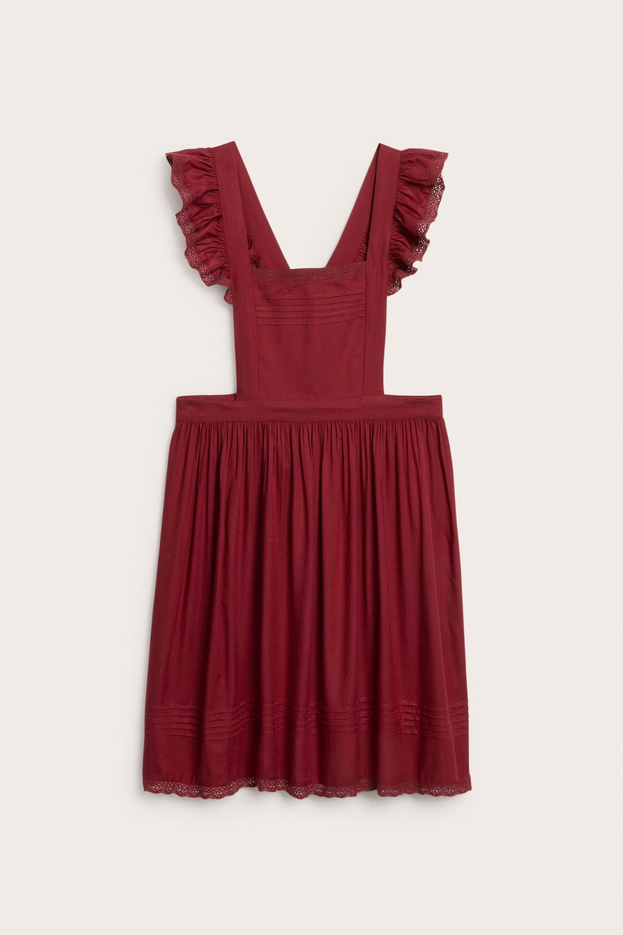 Front view of a red viscose apron dress with ruffled shoulder straps, lace trim, and pintuck details.
