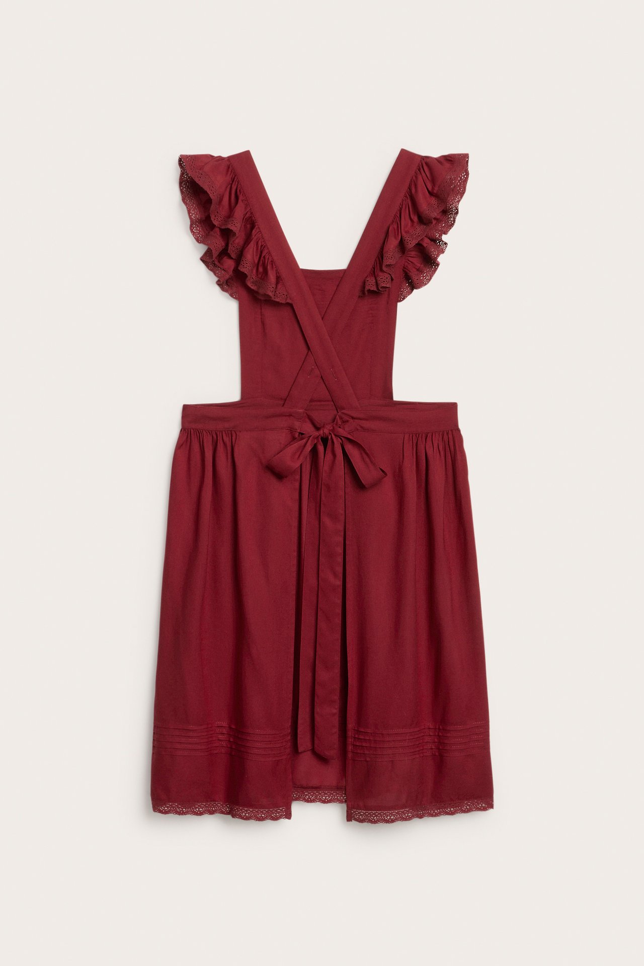 Front view of a red viscose apron dress with ruffled lace shoulder straps and a tie waist.