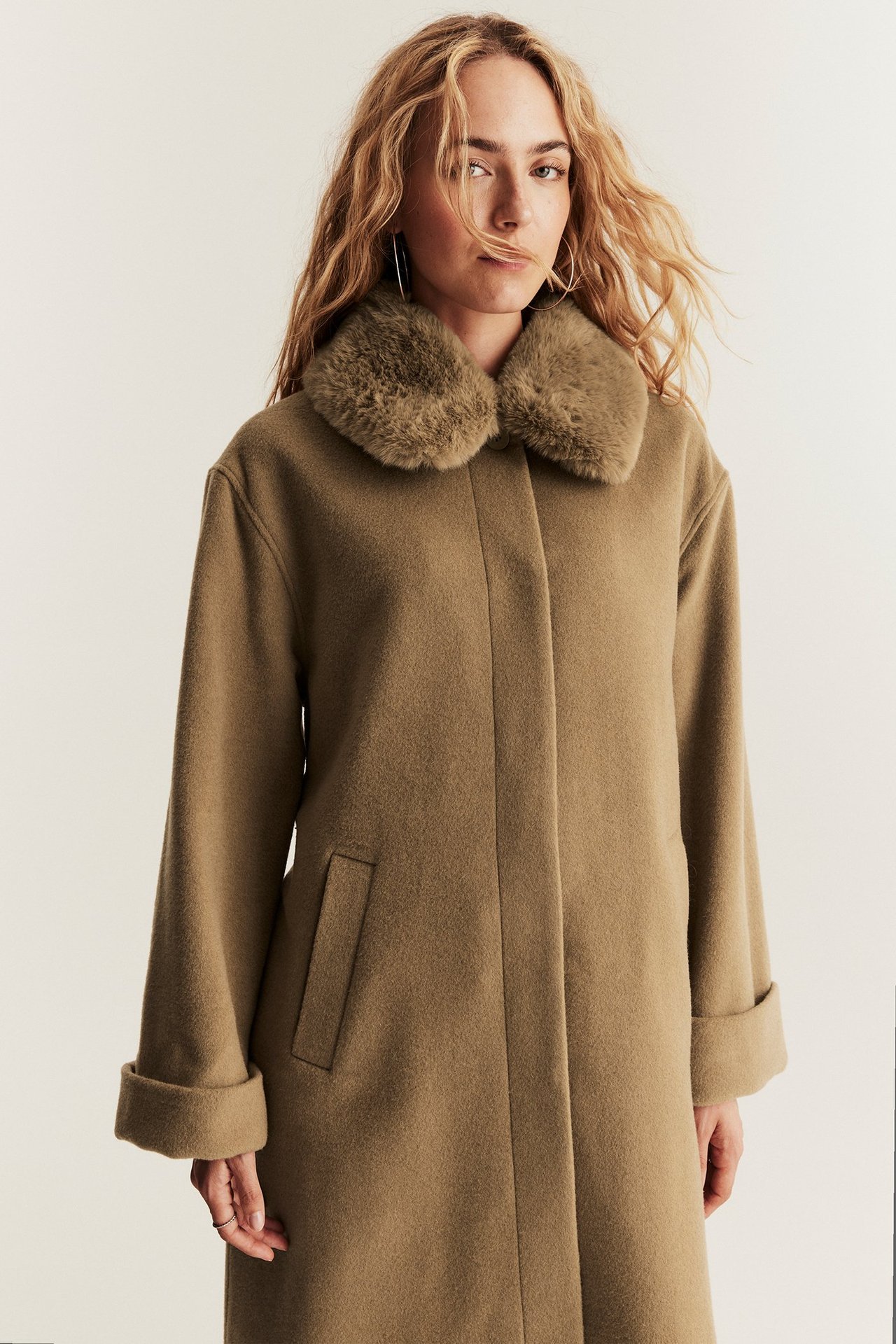Front view of a woman wearing a brown long wool blend coat with a faux fur collar and hidden buttons.