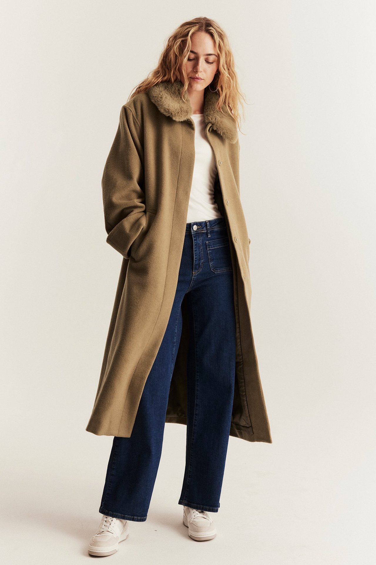 Vorderansicht: Frau trägt offenen braunen Wollmix-Mantel mit Kunstfellkragen, weißes T-Shirt und dunkelblaue Jeans.