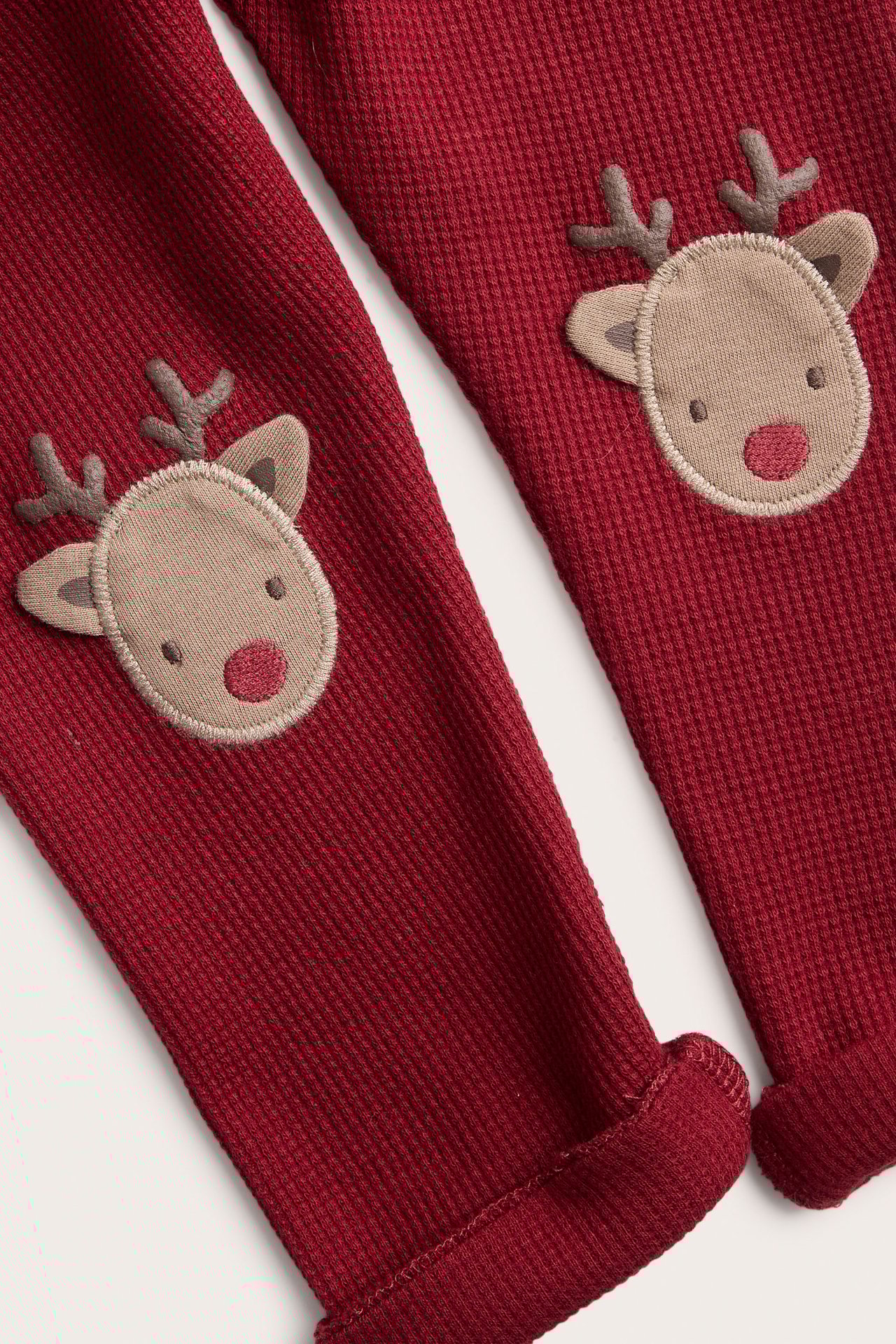 Close-up of kid's dark red waffle-knit leggings with reindeer appliques on knees, rolled cuffs.