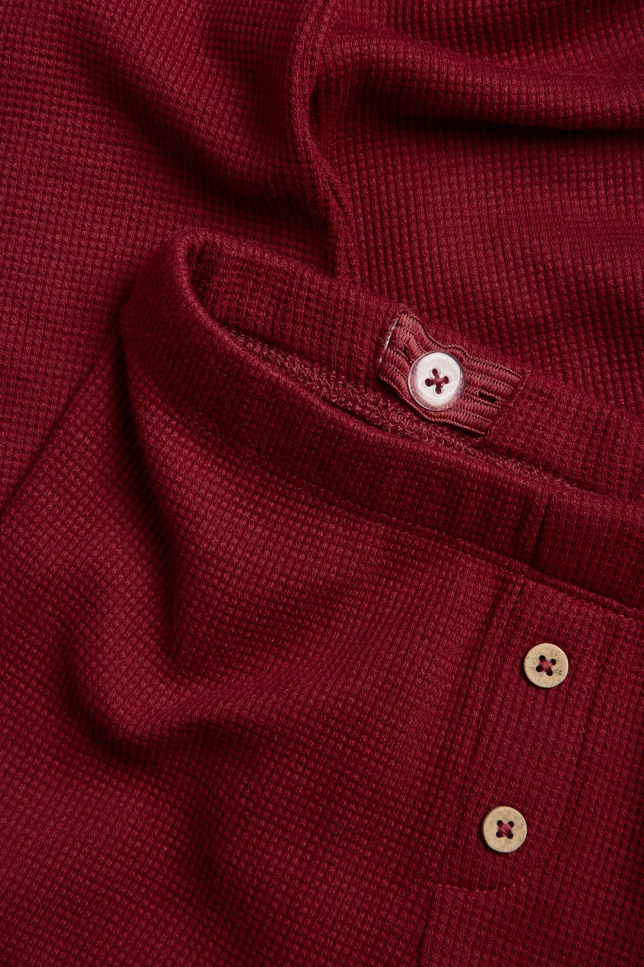 Close-up of kid's dark red waffle leggings with light brown decorative buttons and adjustable waist.