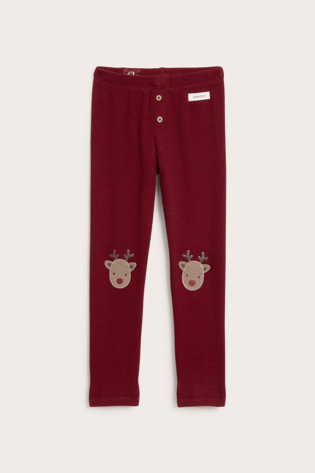 Front view of kid's red waffle-knit leggings with decorative buttons and reindeer appliques on knees.