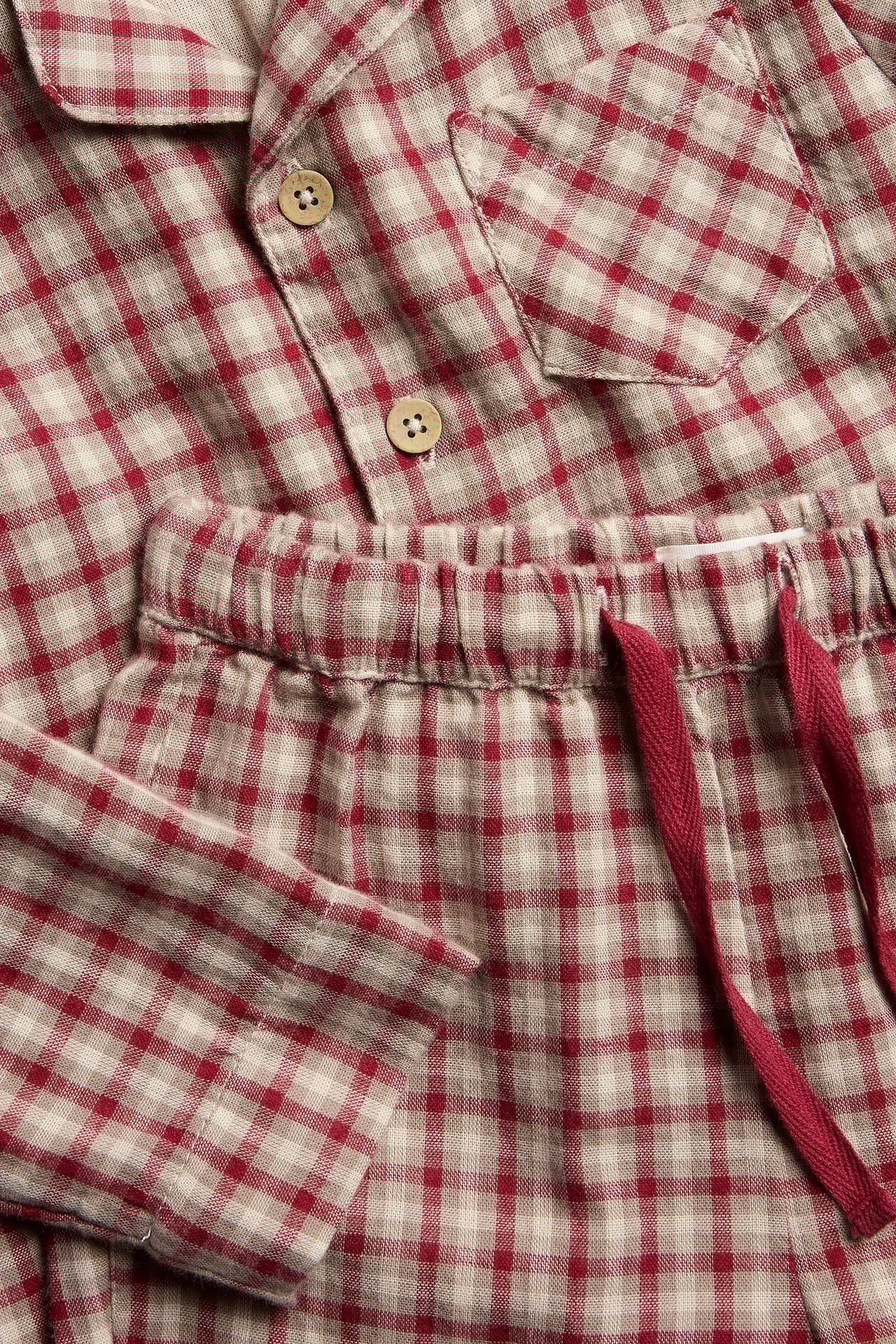 Nahaufnahme eines rot-beigen karierten Baumwollpyjamas. Hemd mit Knöpfen, Hose mit Kordelzug in der Taille.