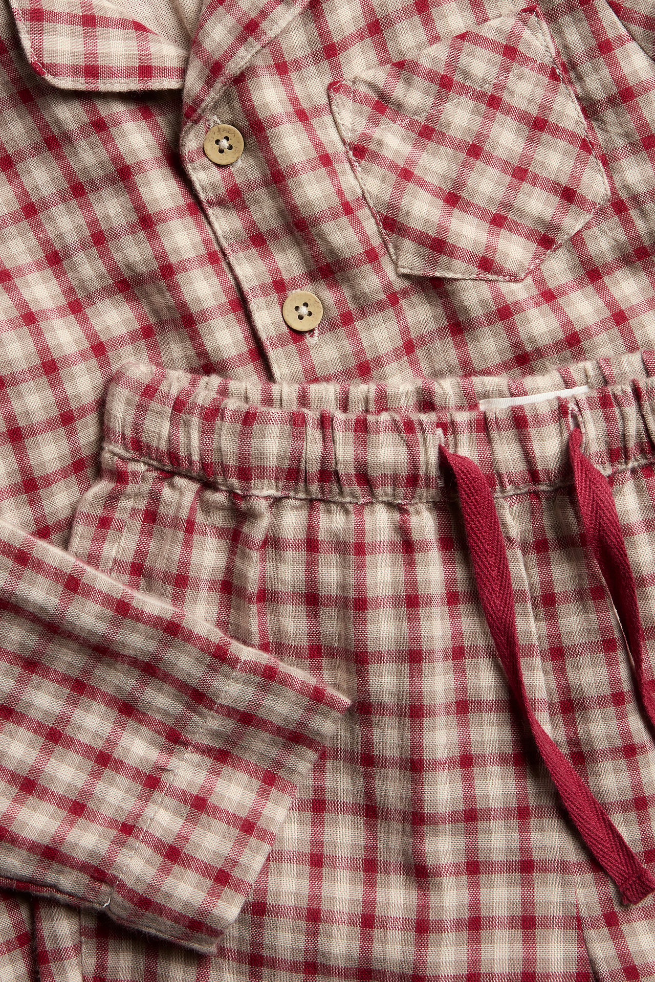 Nahaufnahme eines rot-beigen karierten Baumwollpyjamas. Hemd mit Knöpfen, Hose mit Kordelzug in der Taille.