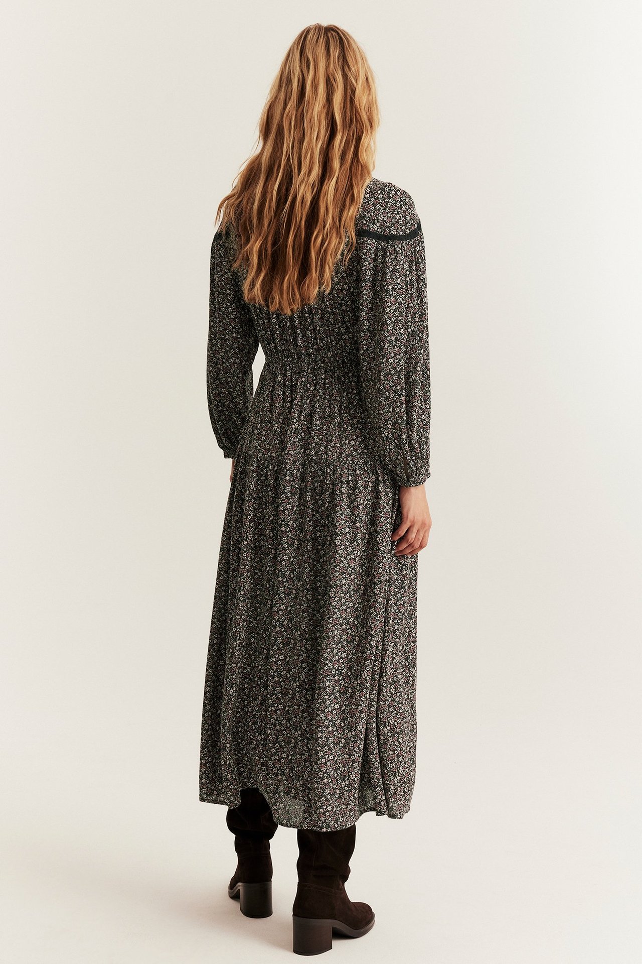 Rückenansicht, Frau in schwarzem geblümtem Viskose-Maxikleid, Puffärmeln und braunen Stiefeln.