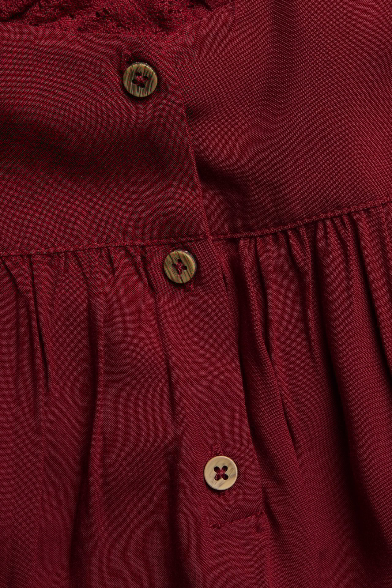 Close-up of a red viscose dress with lace detailing and a button placket featuring three brown buttons.