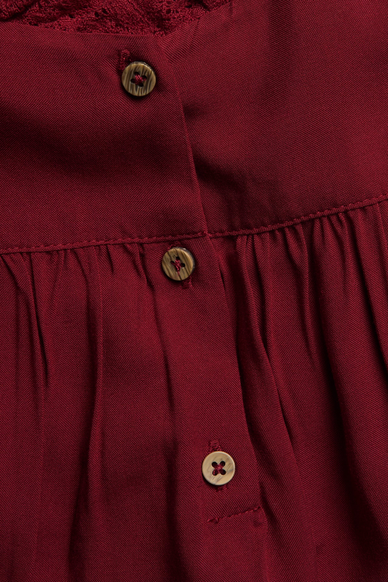 Close-up of a red viscose dress with lace detailing and a button placket featuring three brown buttons.