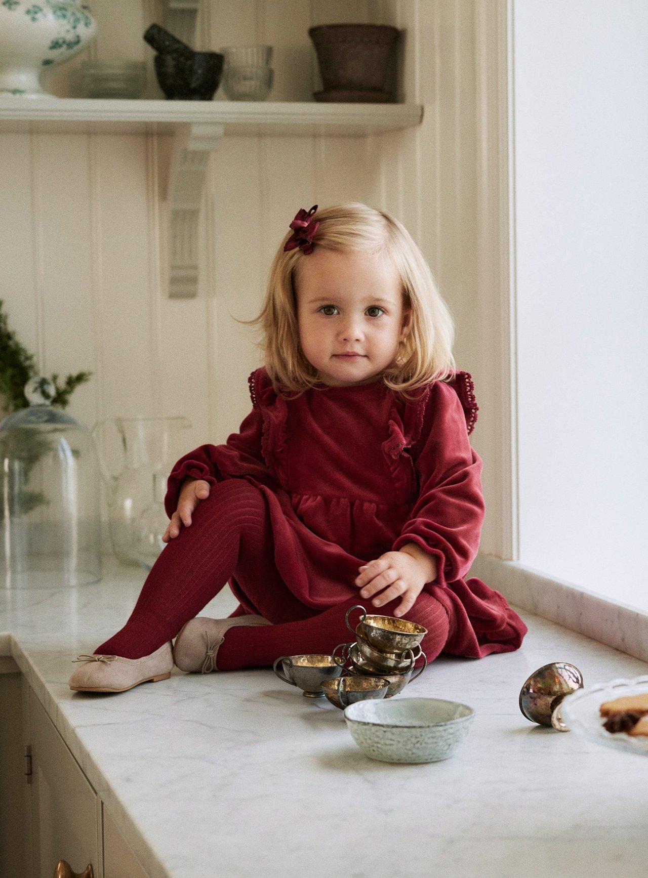 Front view: Kid girl in a dark red viscose dress with lace, matching tights, beige flats, and hair clip.
