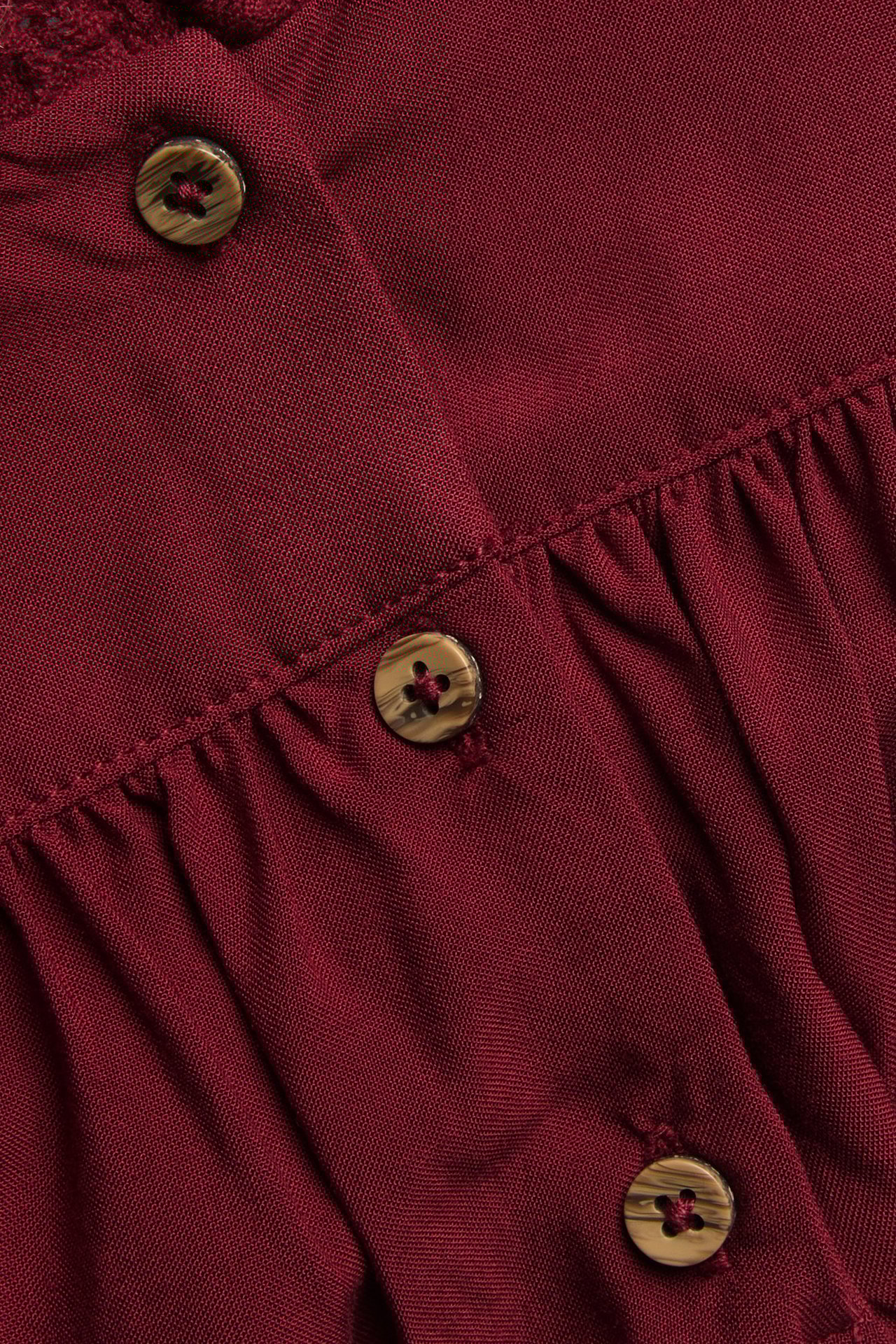 Close-up of a red viscose dress with wooden buttons, gathering, and lace details.