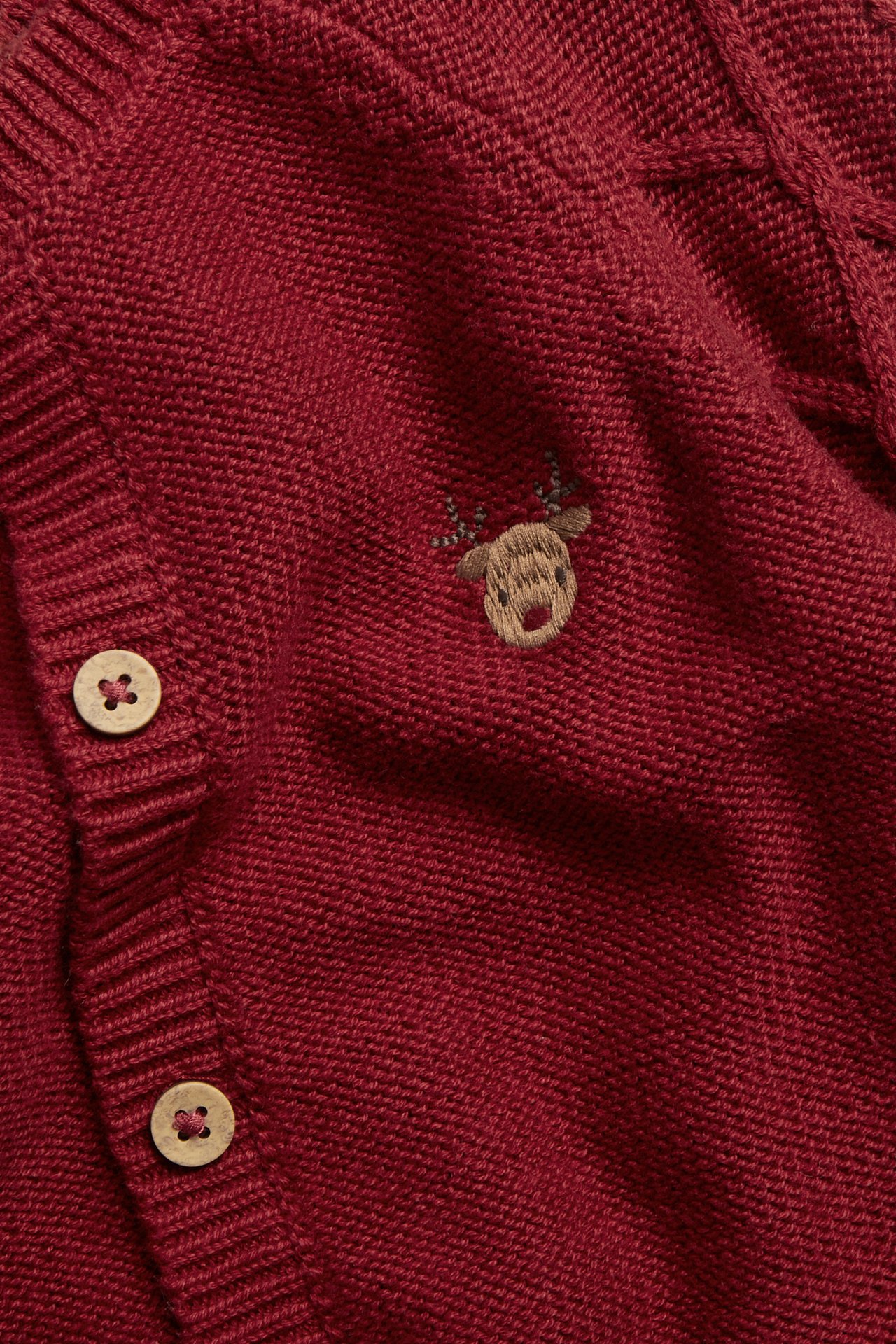 Nahaufnahme einer roten Strickjacke mit Rentierstickerei und Holzknöpfen.