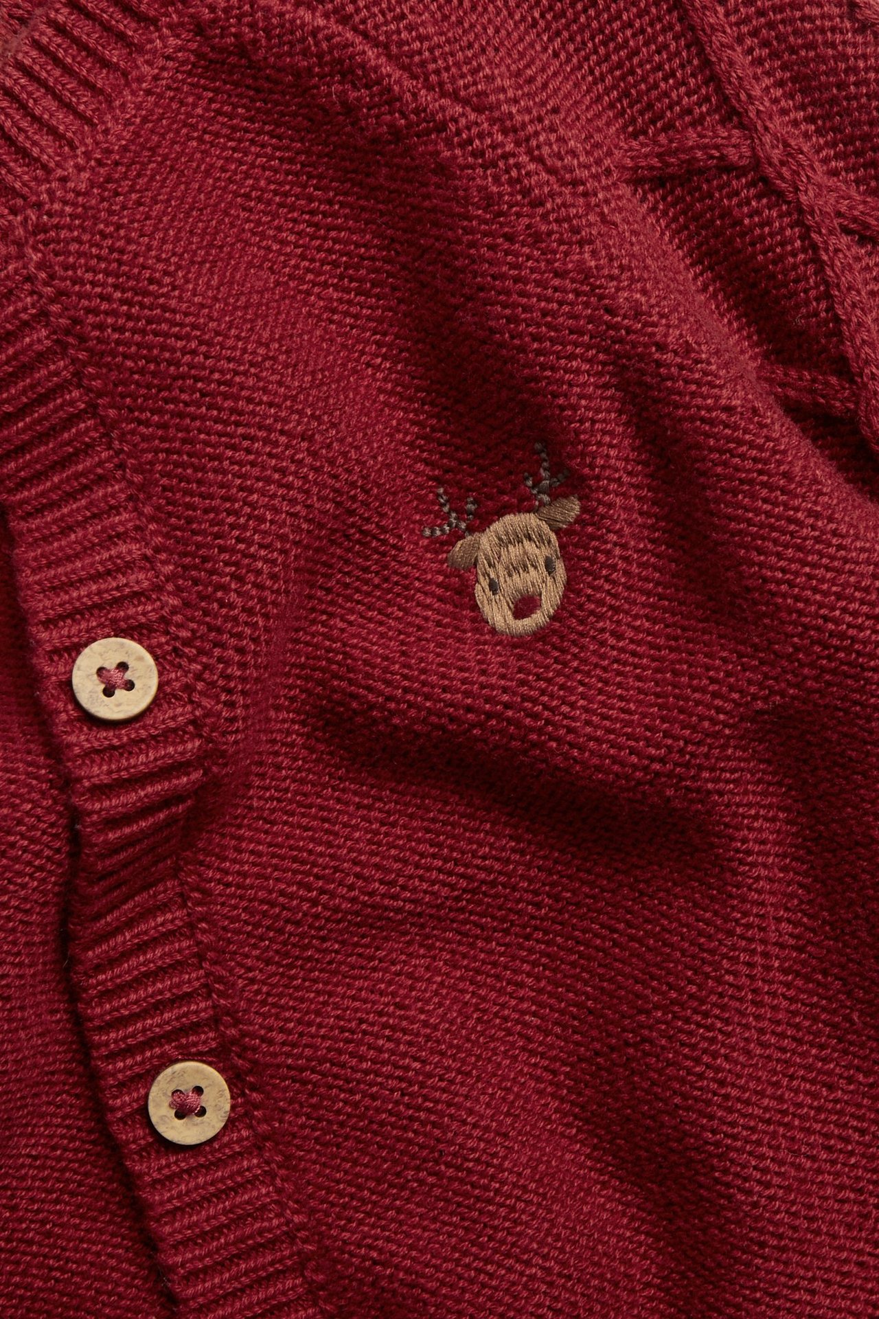 Close-up of a red knitted cotton cardigan with reindeer embroidery, textured sleeves, and wooden buttons.