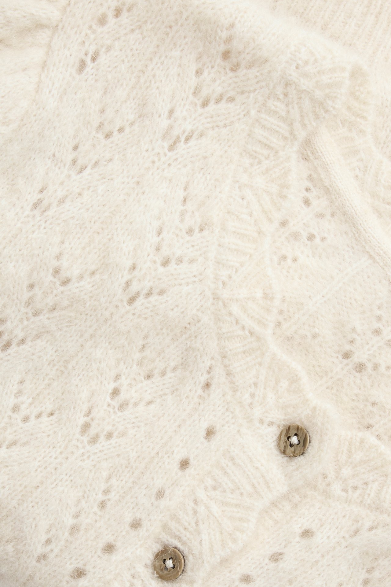 Nahaufnahme einer hellbeigen gemusterten Wollmisch-Strickjacke mit braunen Knöpfen.